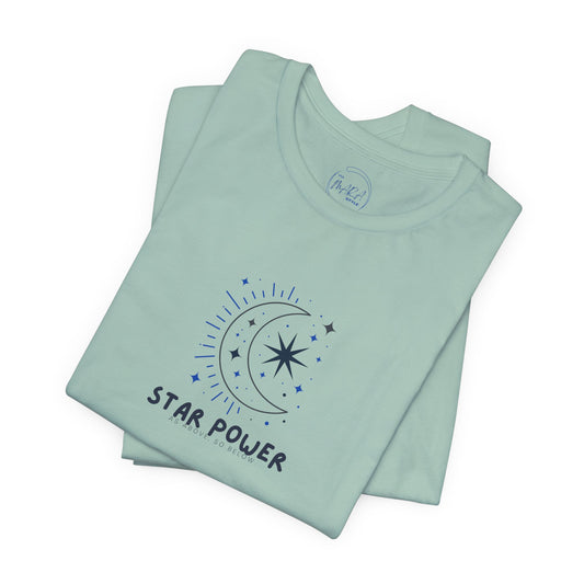 A folded mint green t-shirt with a dark blue graphic of a crescent moon, stars, and the text 'STAR POWER' on the front, set against a plain white background.