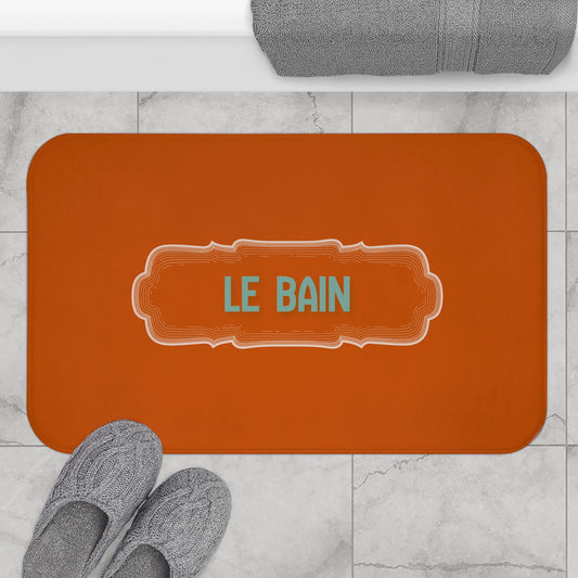Orange bath mat with 'LE BAIN' text on a marble floor with slippers and a towel.