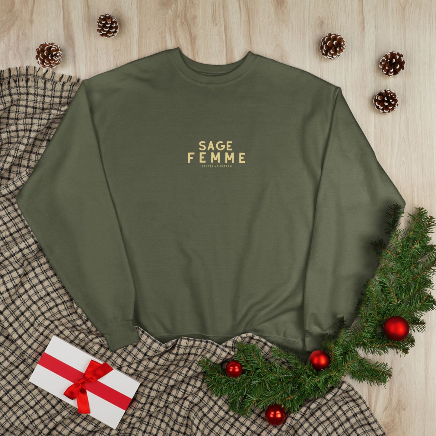 Green sweatshirt with 'SAGE FEMME' text on a wooden surface with Christmas decorations.