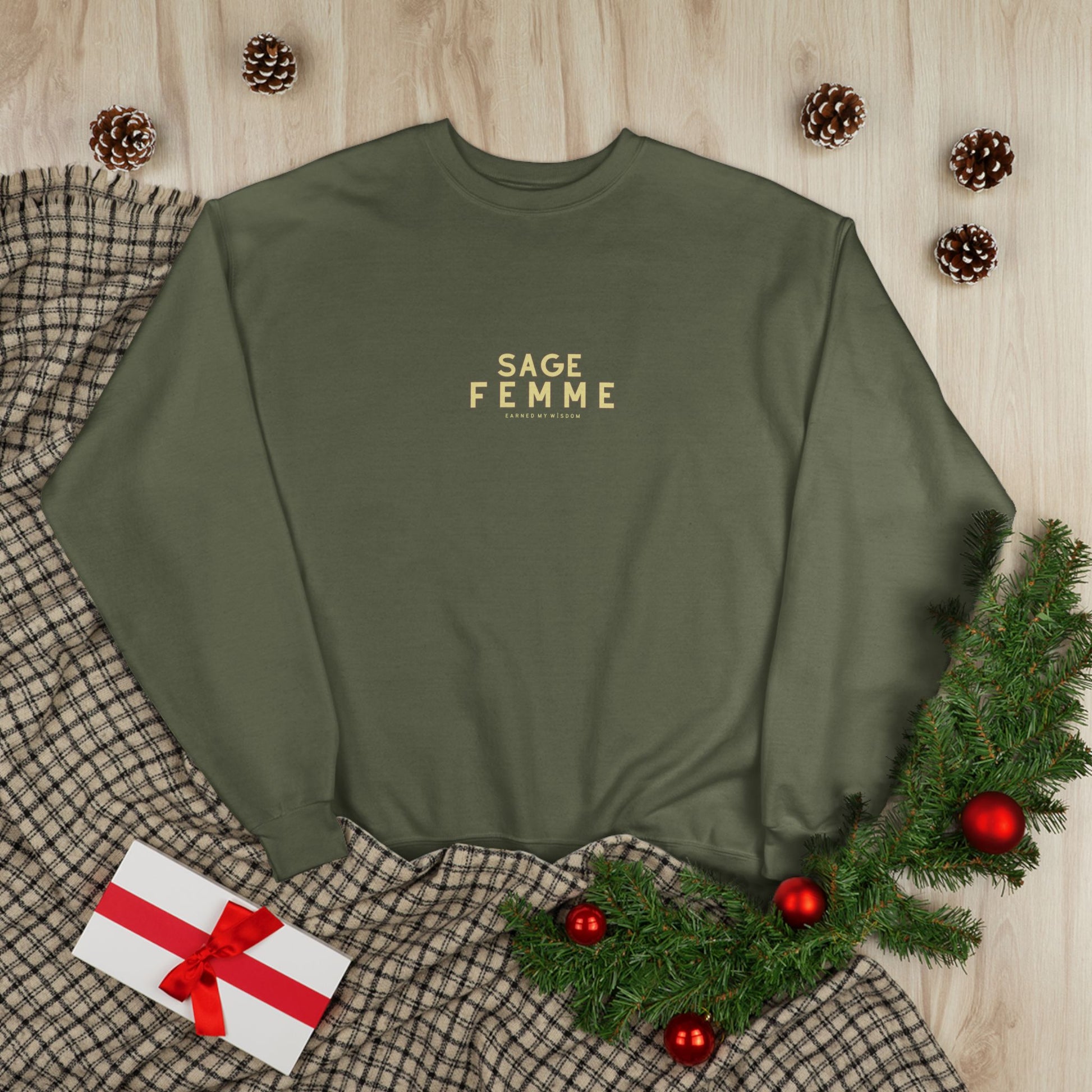 Green sweatshirt with 'SAGE FEMME' text on a wooden surface with Christmas decorations.