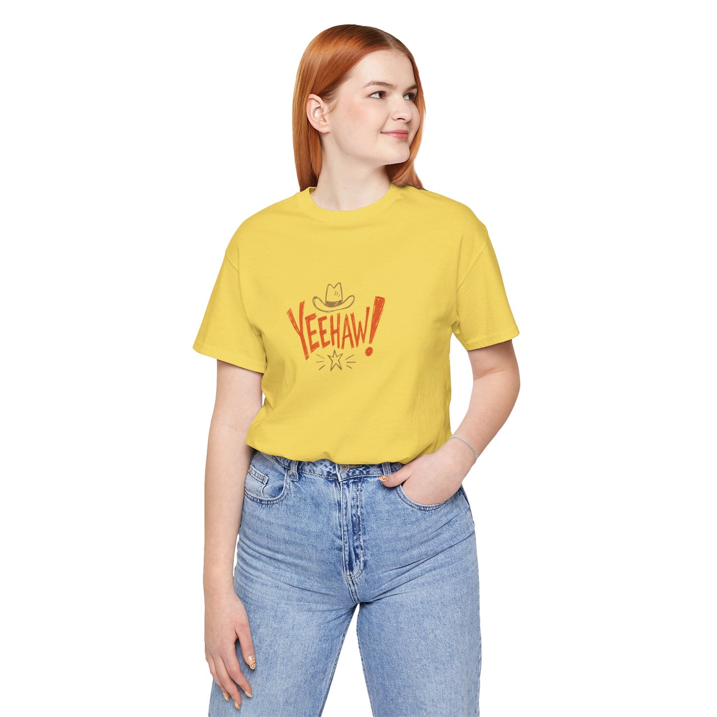 A young woman with red hair wearing a yellow graphic t-shirt with 'VEEHAW!' printed in red and orange, paired with light blue jeans, against a plain white background.