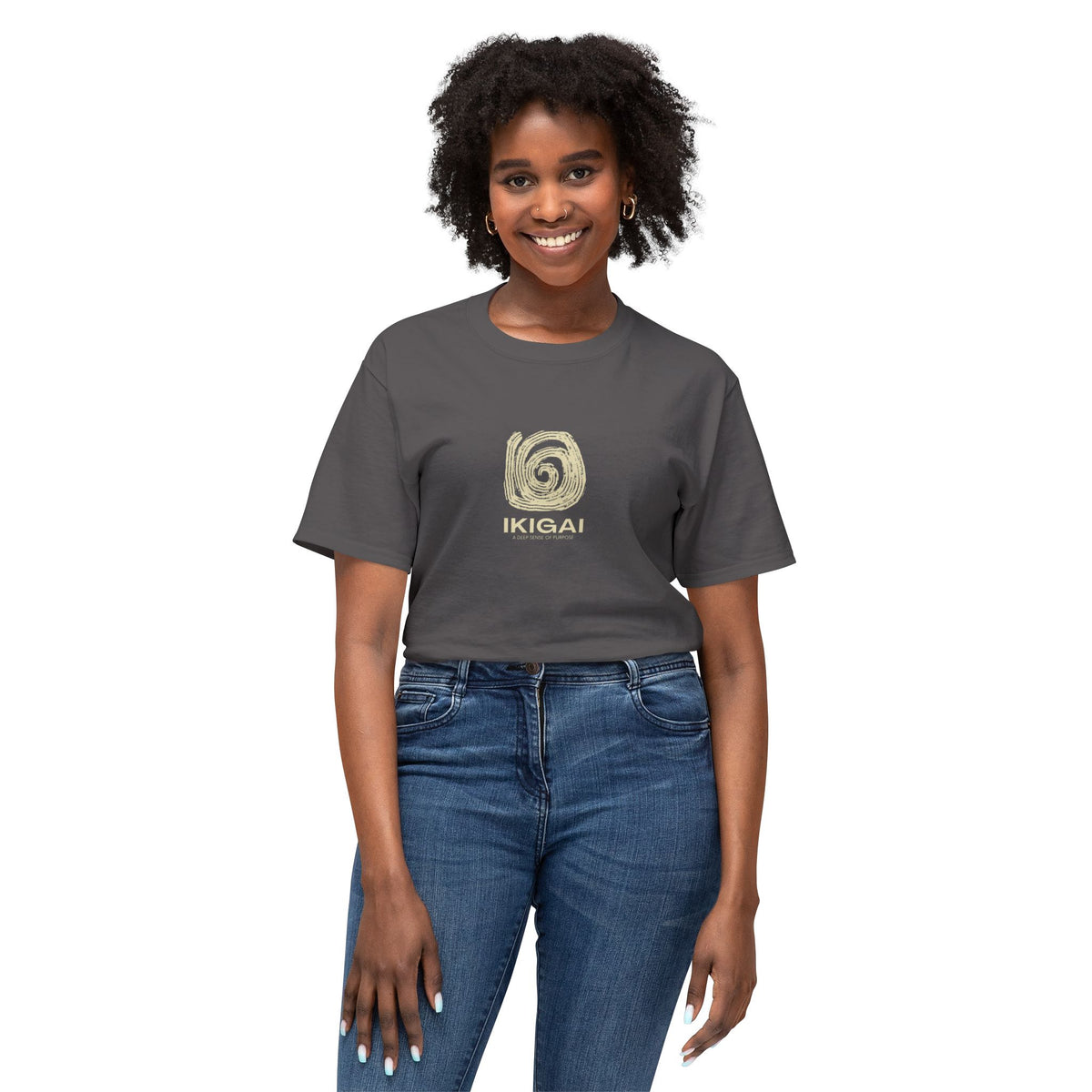 A woman modeling a dark gray crewneck t-shirt with a gold spiral graphic and the word 'IKIGAI' printed on the chest, paired with blue jeans against a plain white background.