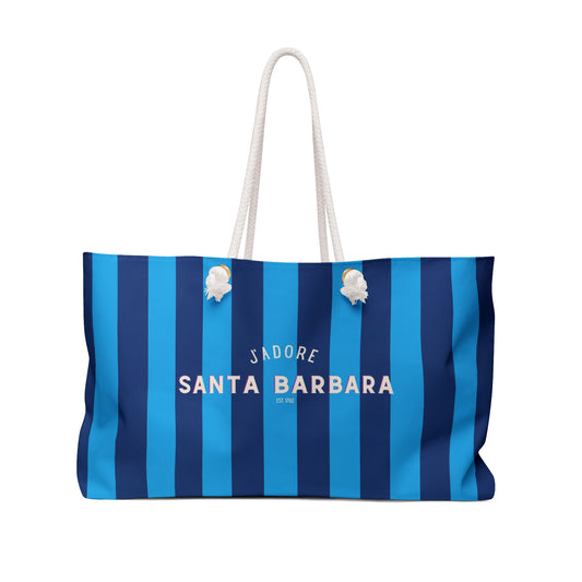 A striped tote bag with vertical blue and navy stripes, featuring white rope handles and the text 'SANTA BARBARA' printed in white on the front.