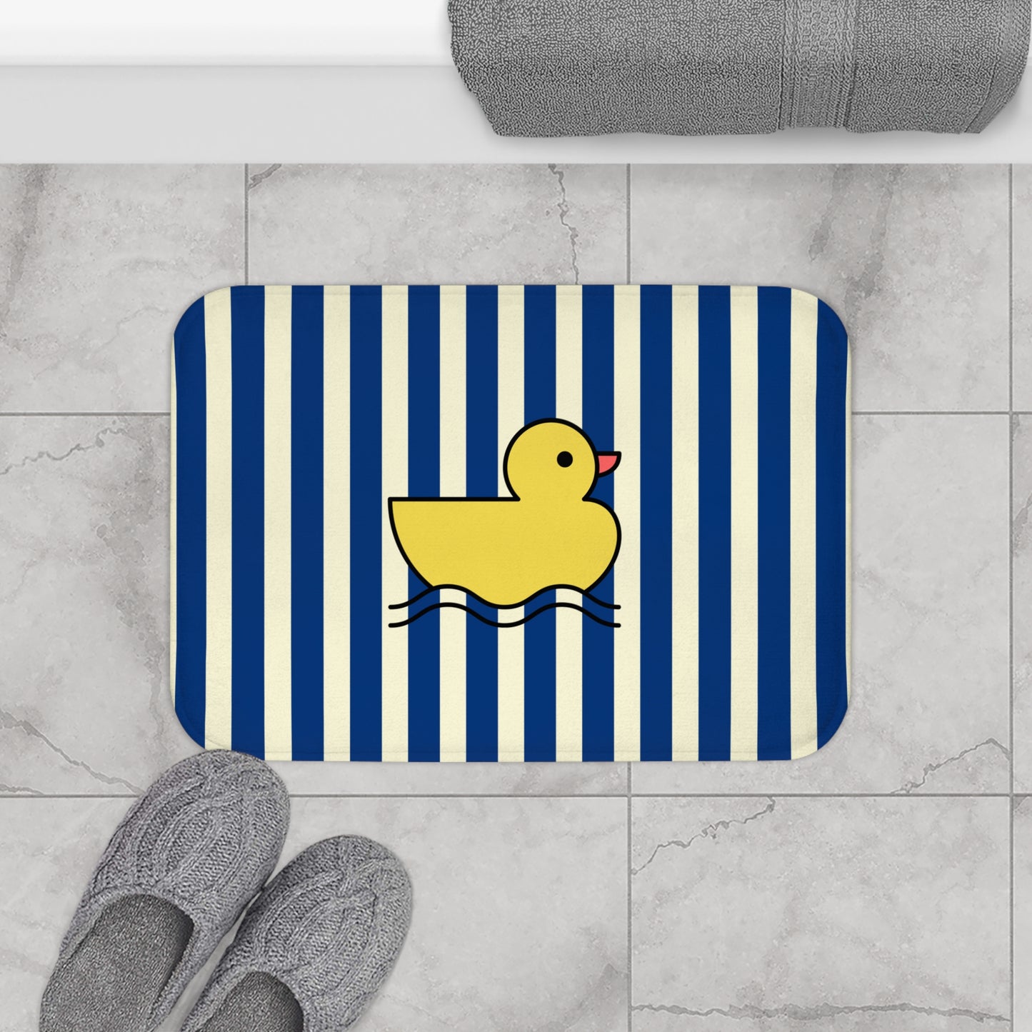 Bath mat with a yellow rubber duck on a blue and white striped background, placed on a tiled floor.