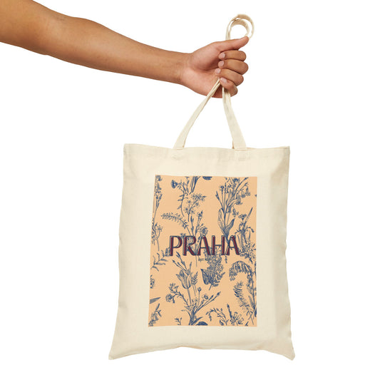 Tote bag with floral design and 'PRAHA' text held by a hand on a white background