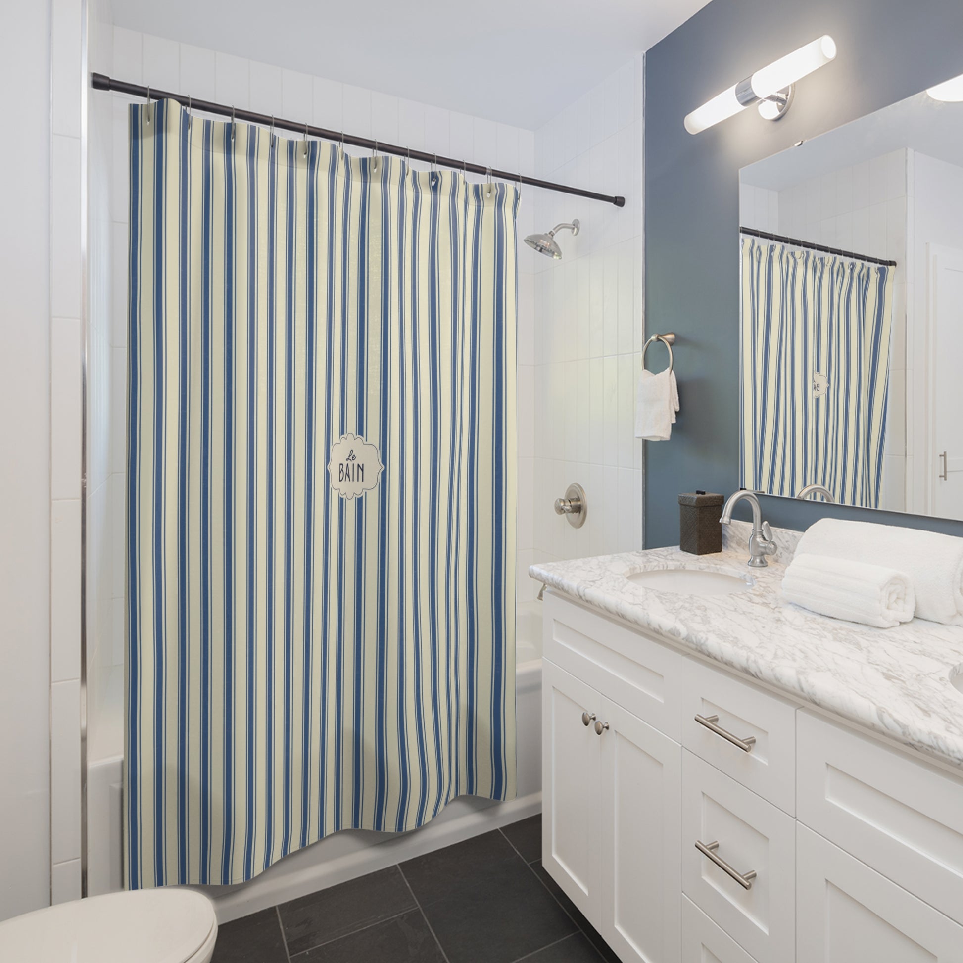 A blue and white vertically striped shower curtain hanging in a modern bathroom with a white vanity, marble countertop, and a blue accent wall.