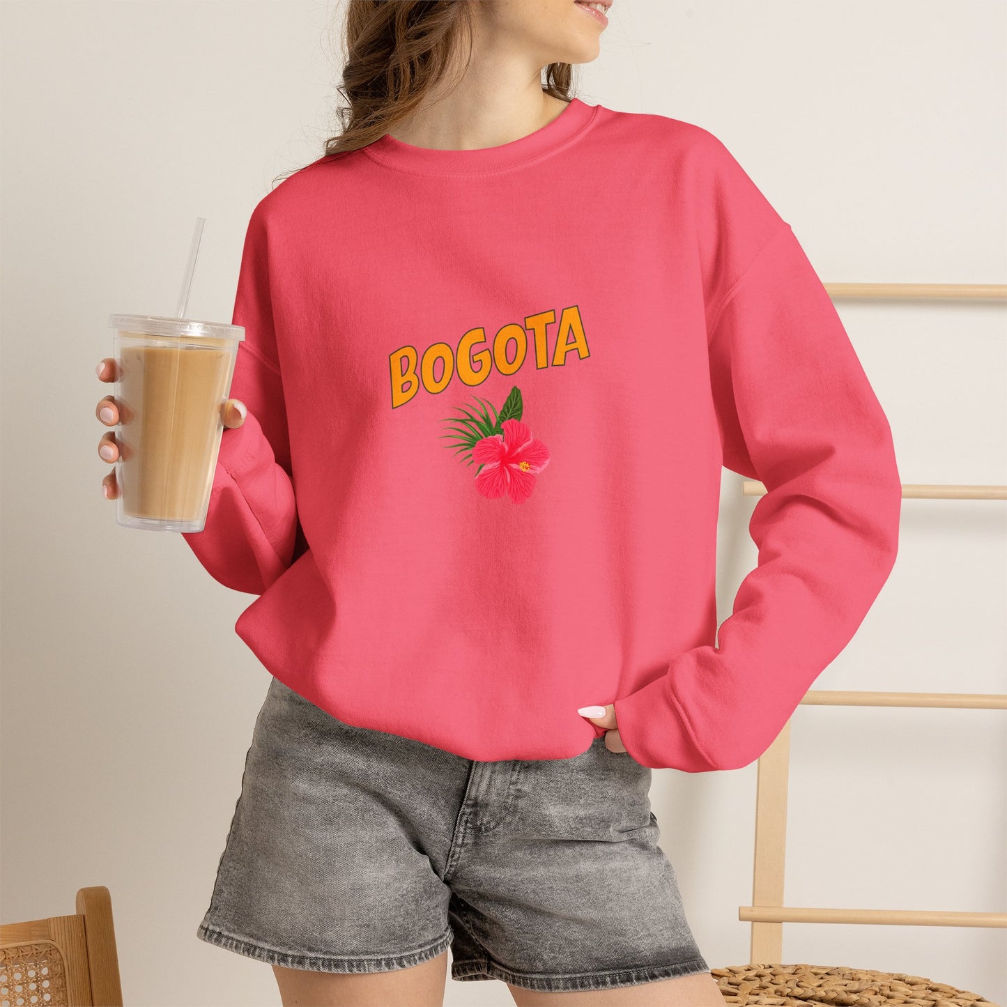 Person wearing a pink sweatshirt with 'BOGOTA' and a flower design, holding a drink.