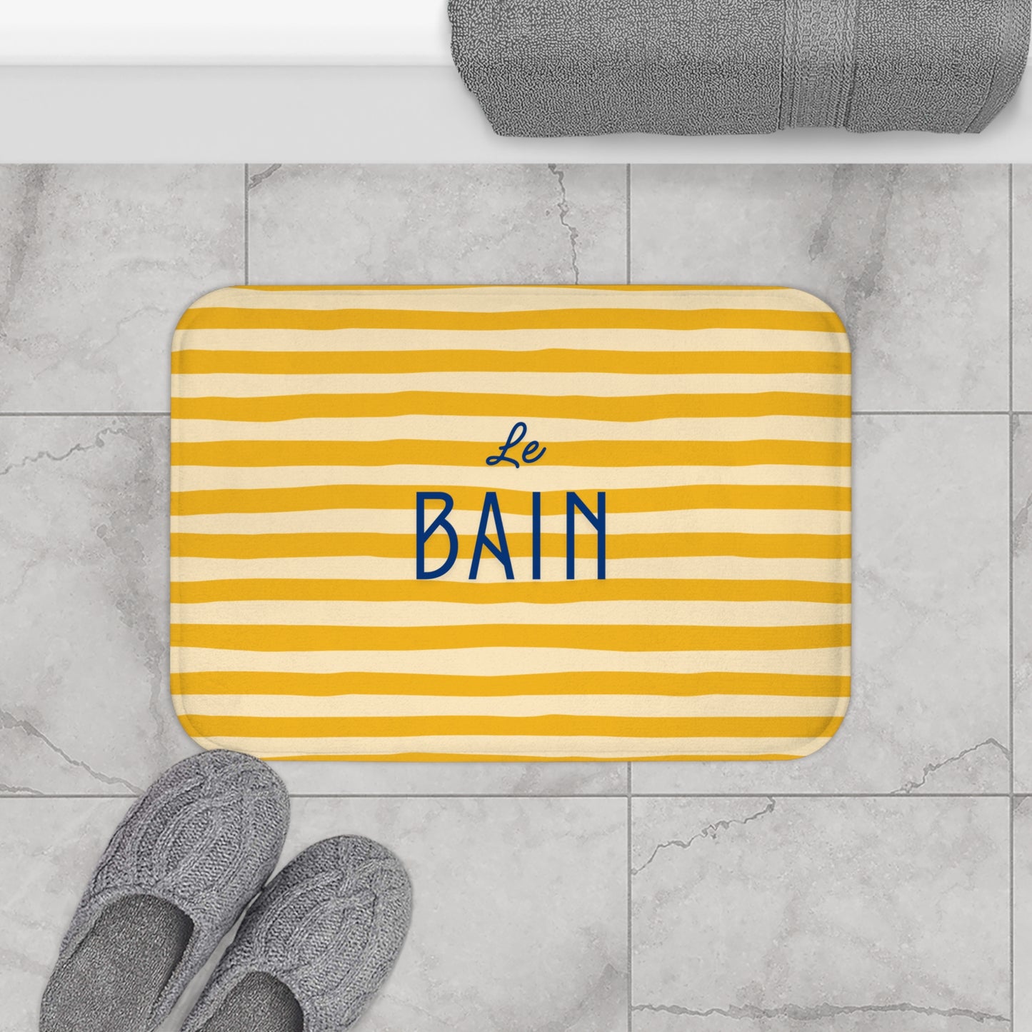 Yellow striped bath mat with 'Le Bain' text on a marble floor.