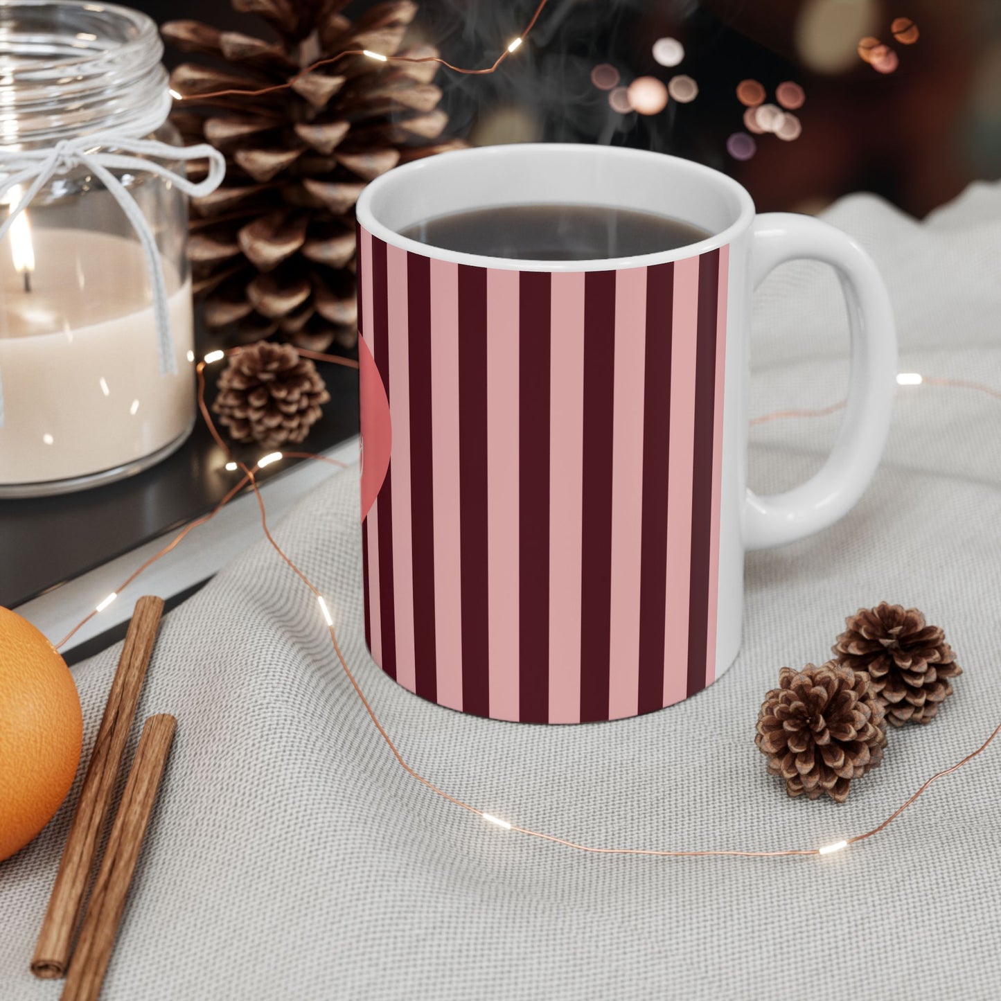 Striped mug with a warm setting of a candle, oranges, and pinecones.