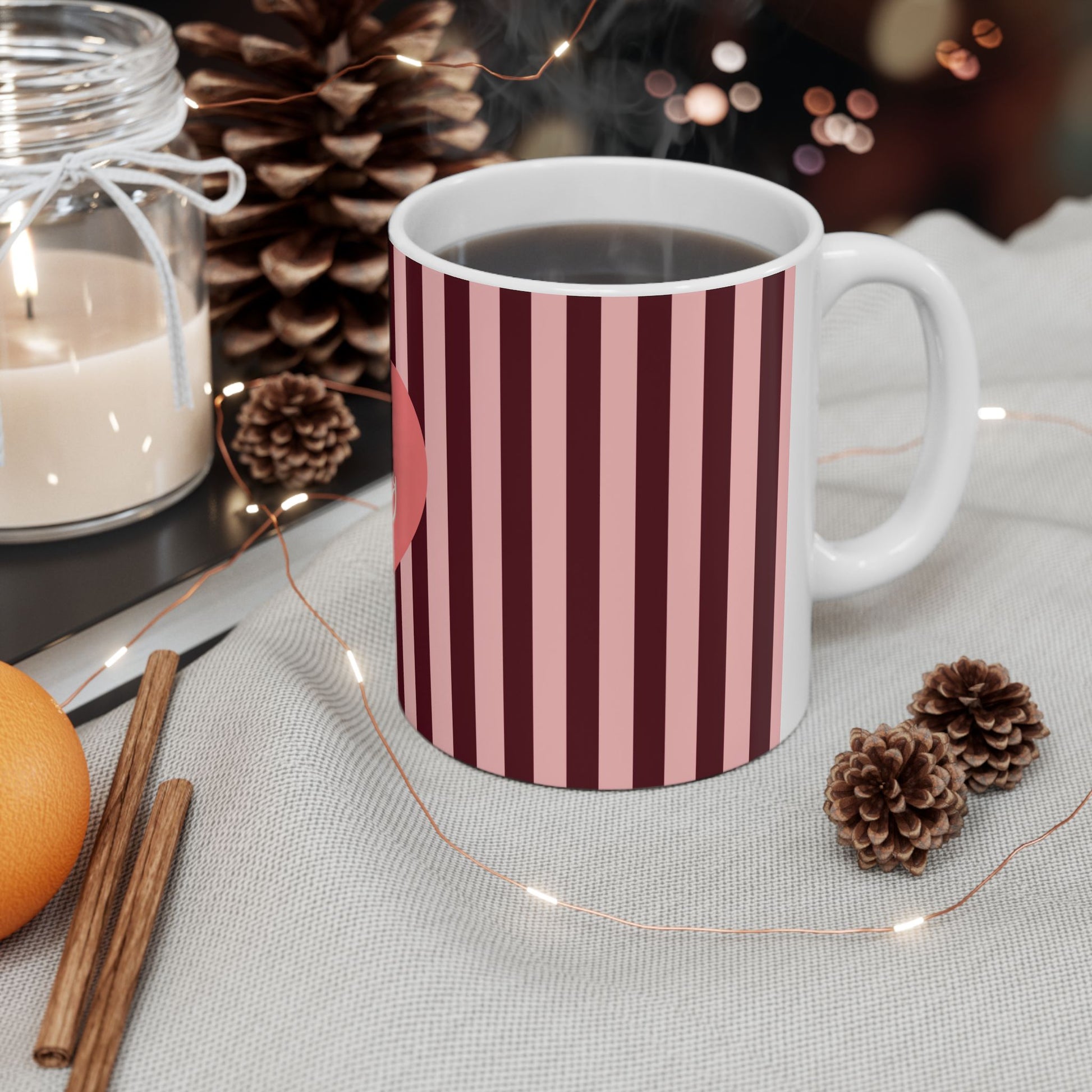 Striped mug with a warm setting of a candle, oranges, and pinecones.