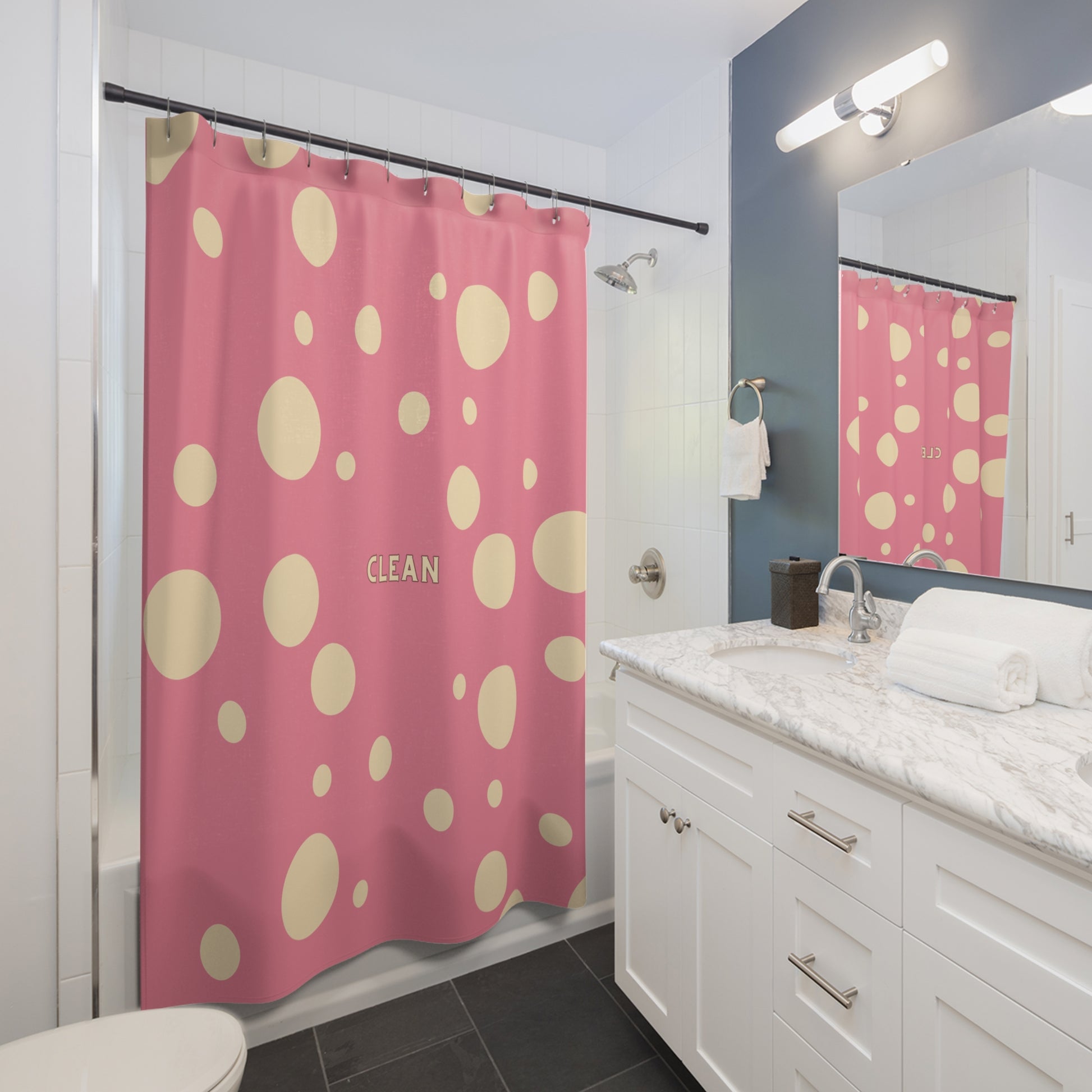 A pink shower curtain with large beige polka dots and the word 'CLEAN' printed in the center, shown hanging in a modern white bathroom with a marble countertop, mirror, and dark gray floor.