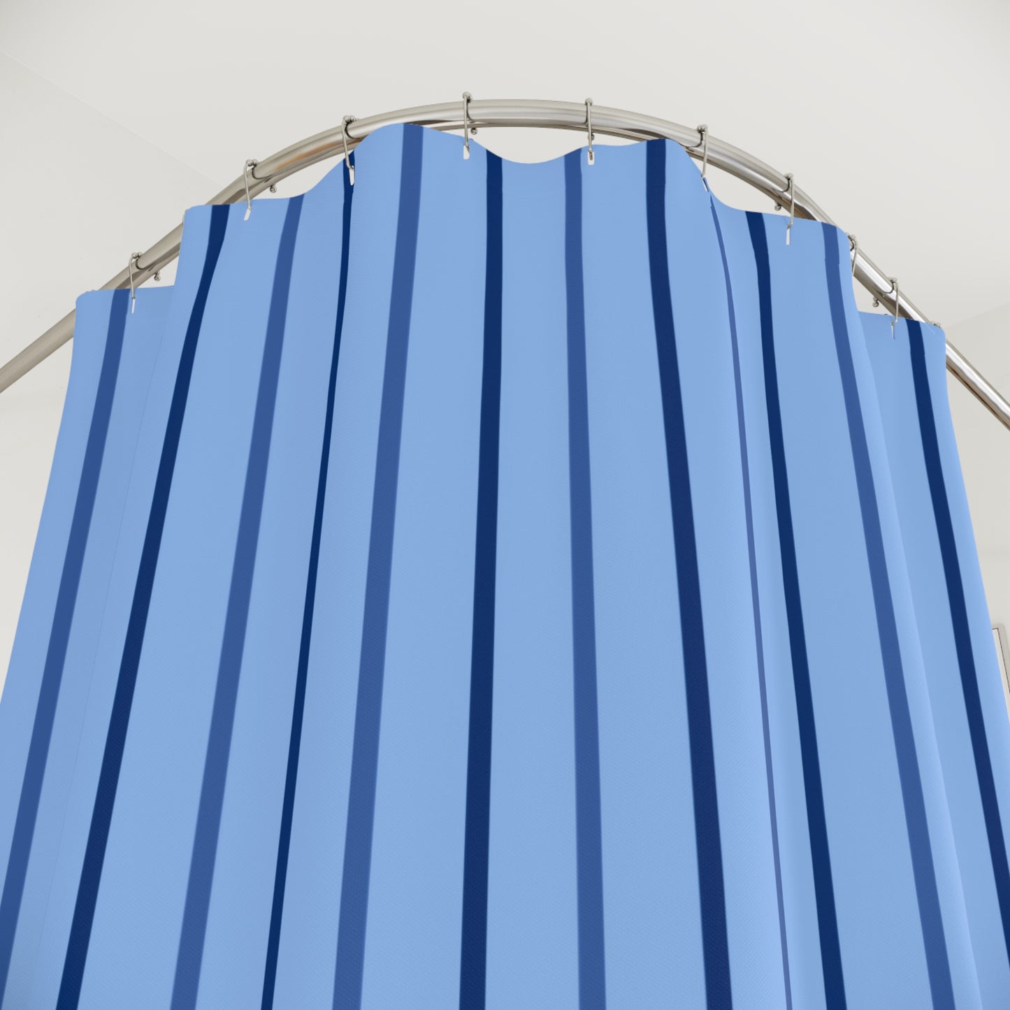 A light blue fabric curtain with vertical dark blue stripes, hanging from a curved silver metal rod against a plain white wall.