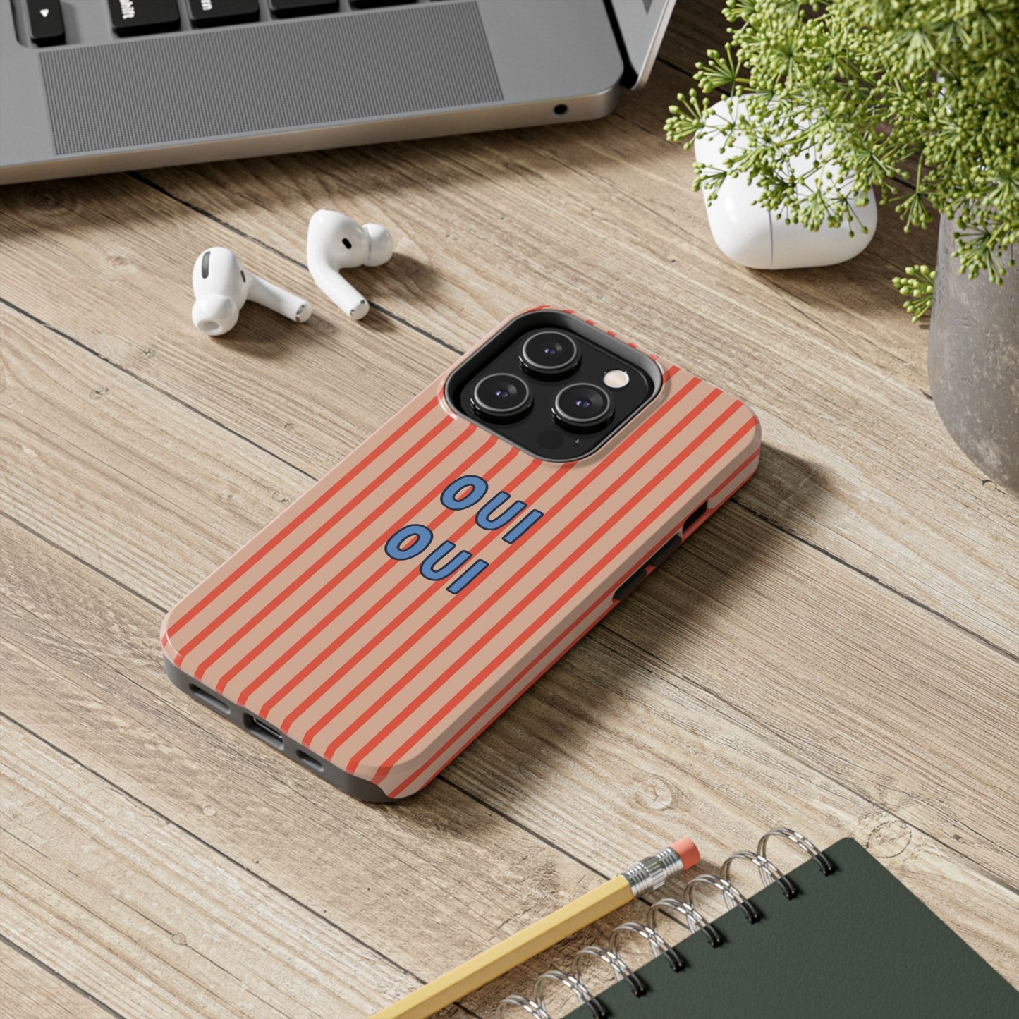Phone case with 'OUI' text on a wooden surface with laptop, earbuds, and notebook.