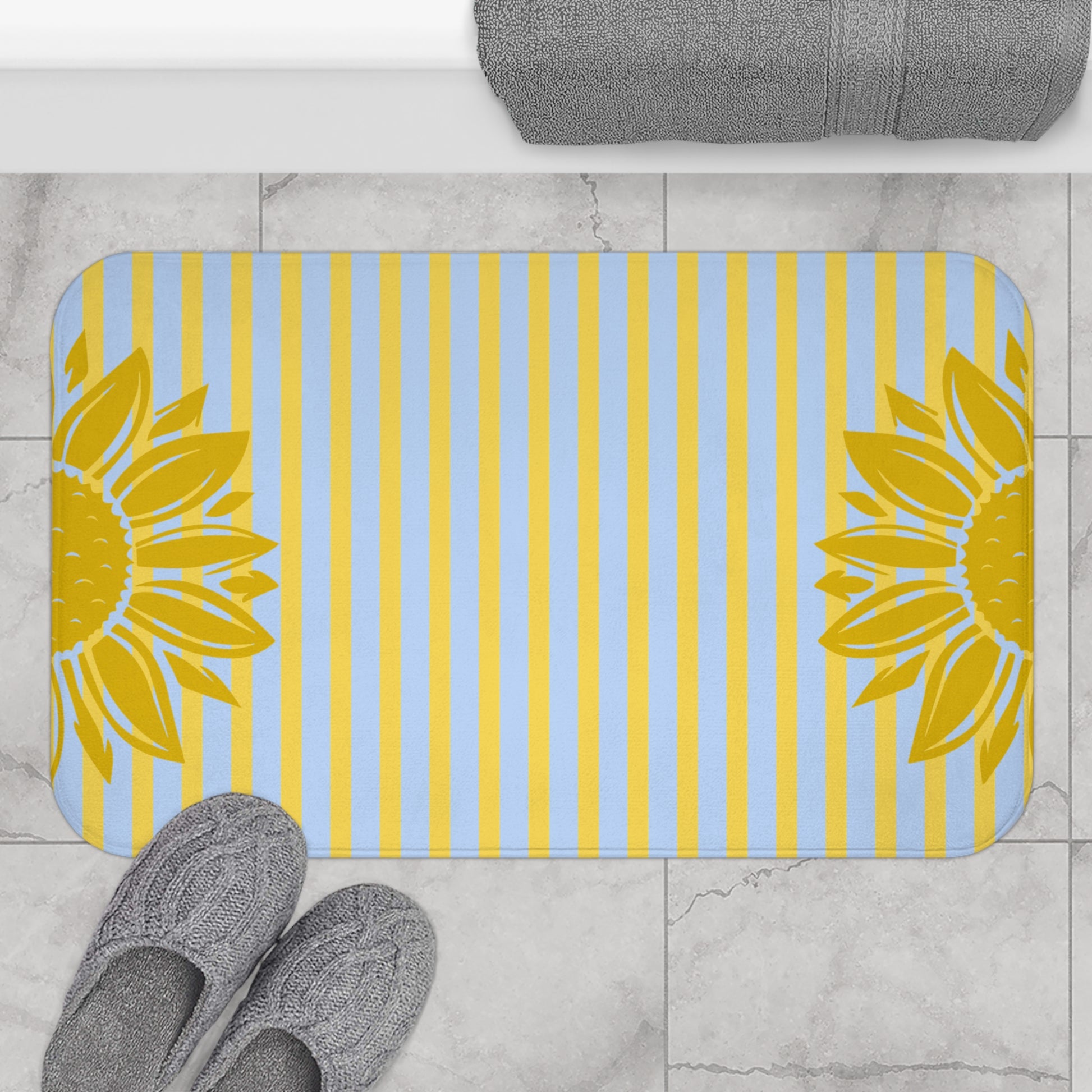 Bath mat with sunflower design on a striped pattern, placed on a tiled floor.