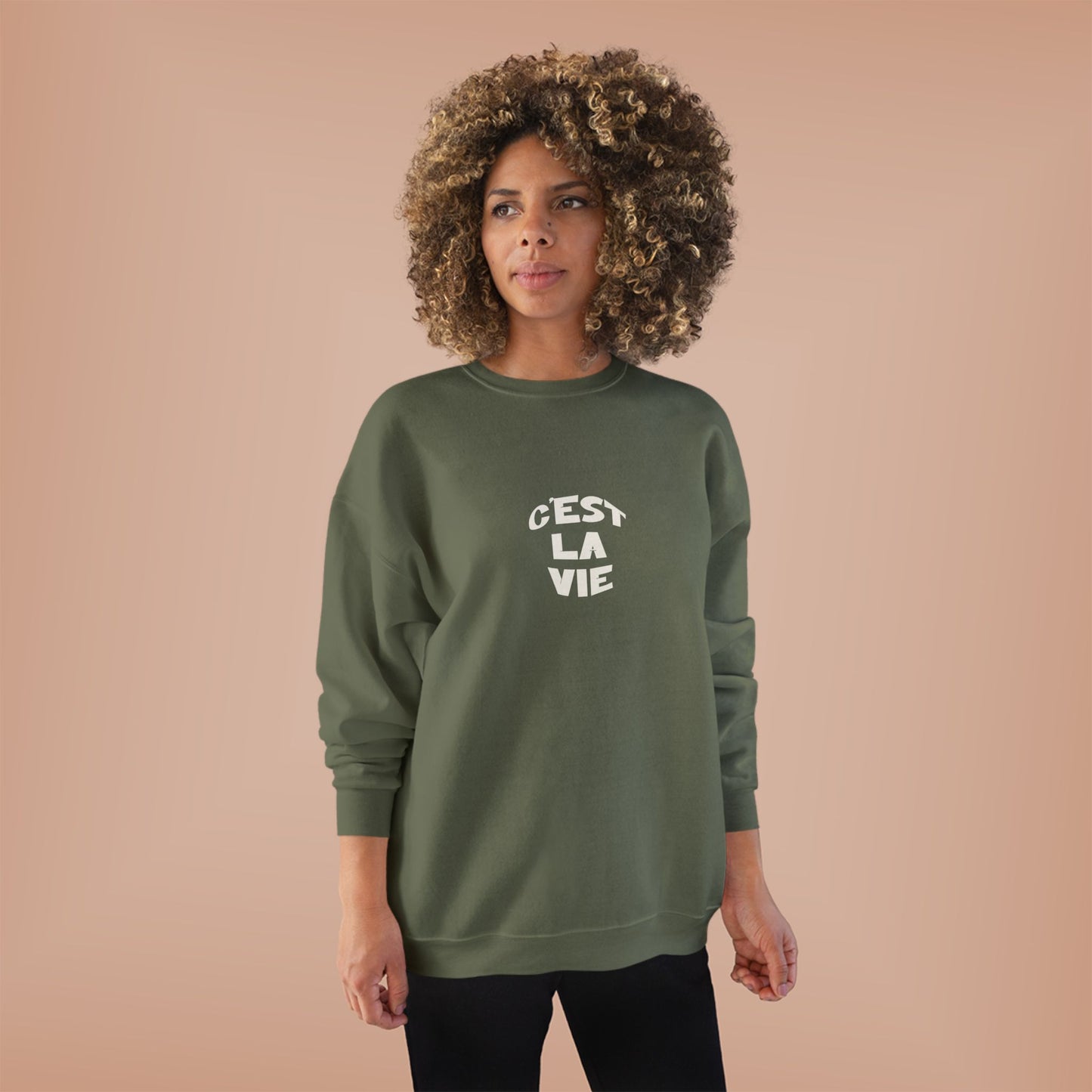Woman wearing a green sweatshirt with 'Cést La Vie' text on a beige background