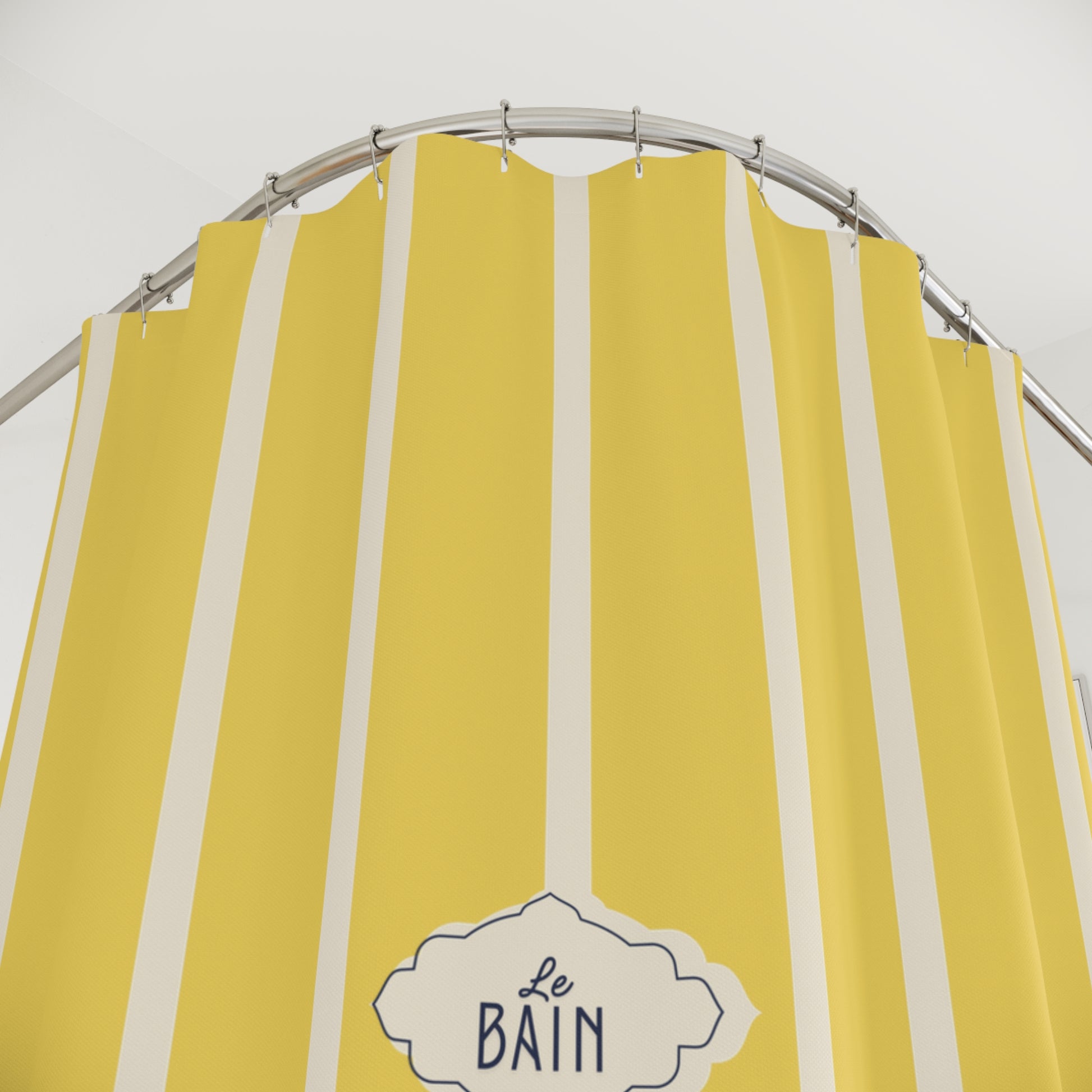 Yellow and white vertically striped shower curtain with a metal curved rod and a decorative label reading 'Le Bain'.