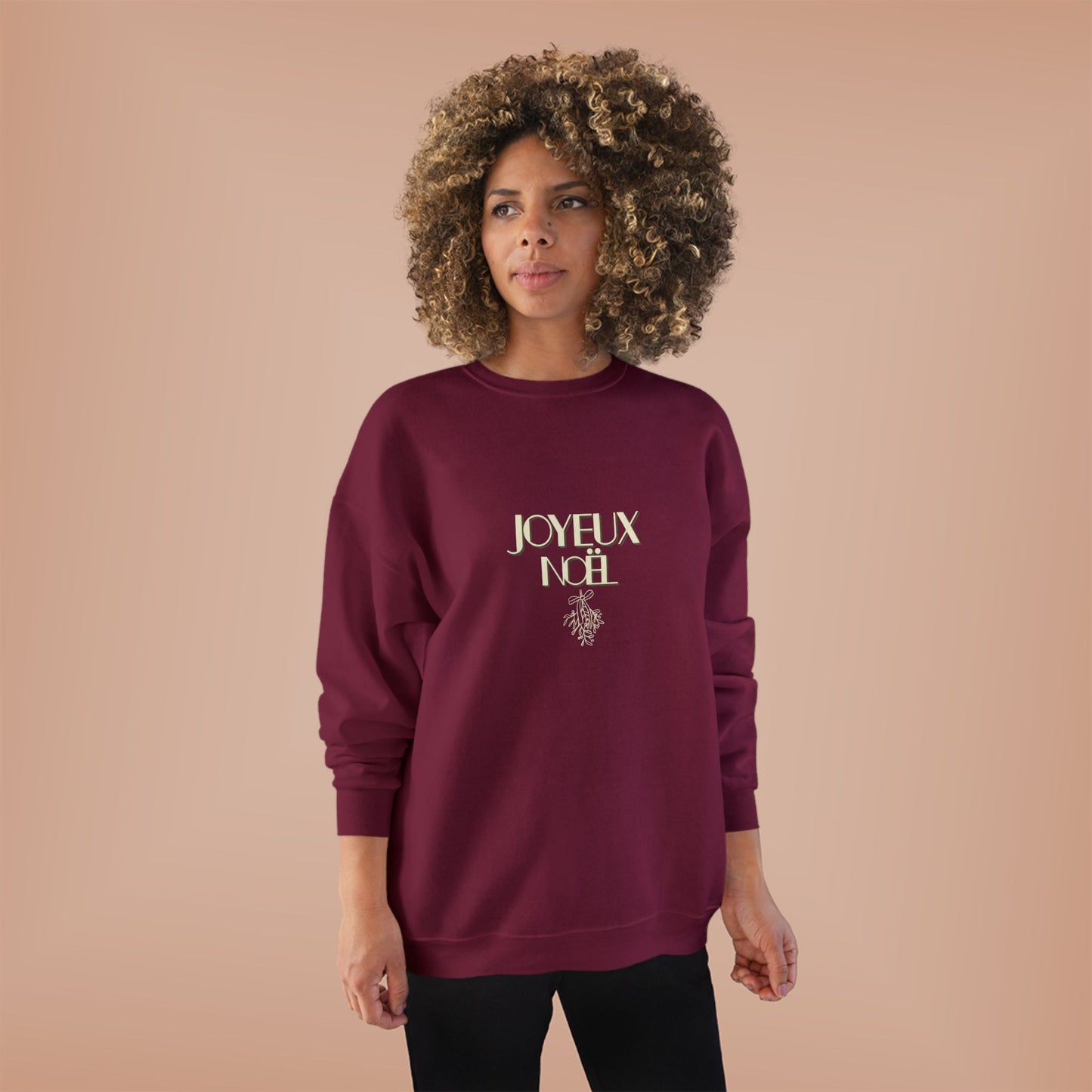 Woman wearing a burgundy sweatshirt with 'JOYEUX NOEL' text on a beige background