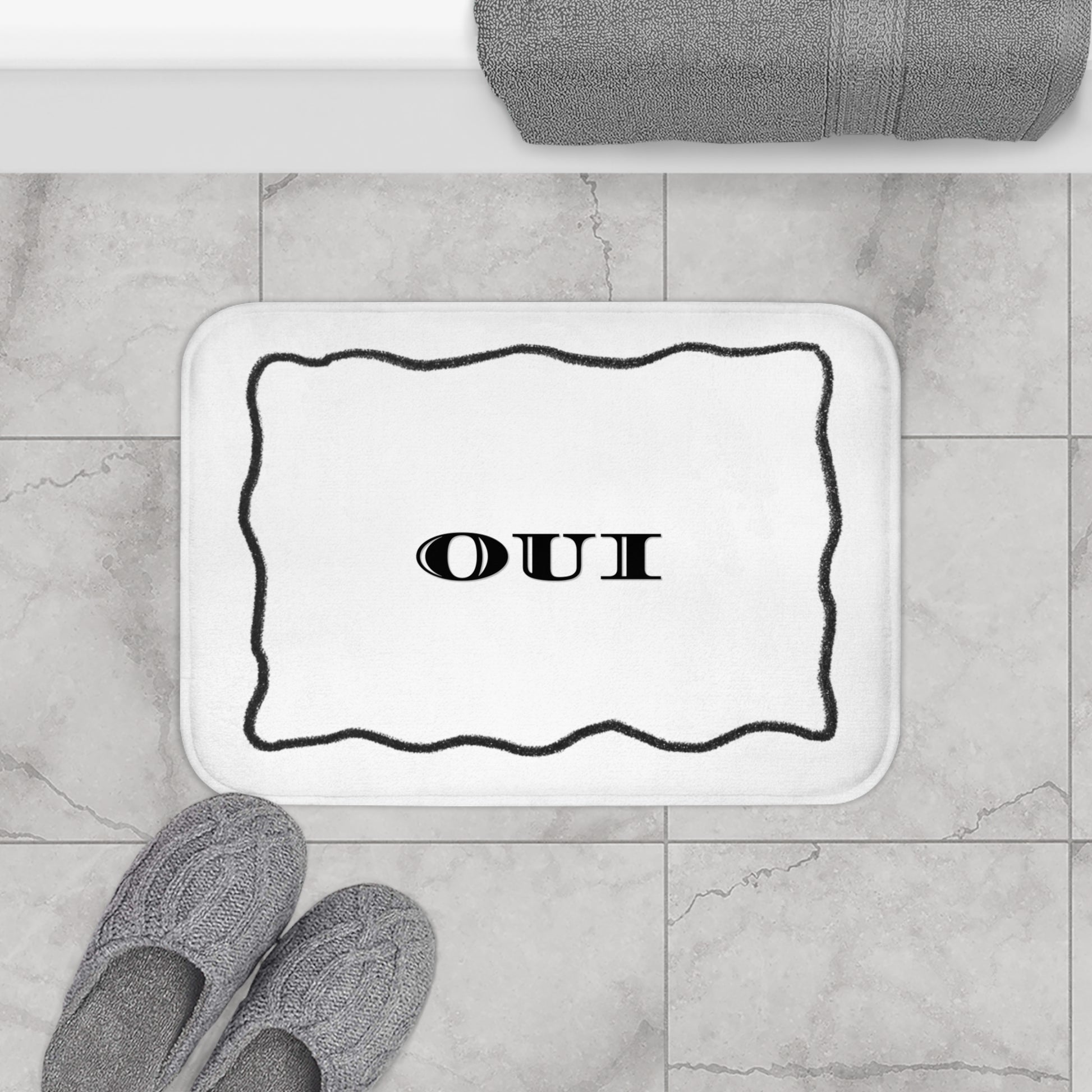 Bath mat with 'OUI' text on a bathroom floor with slippers and towel.