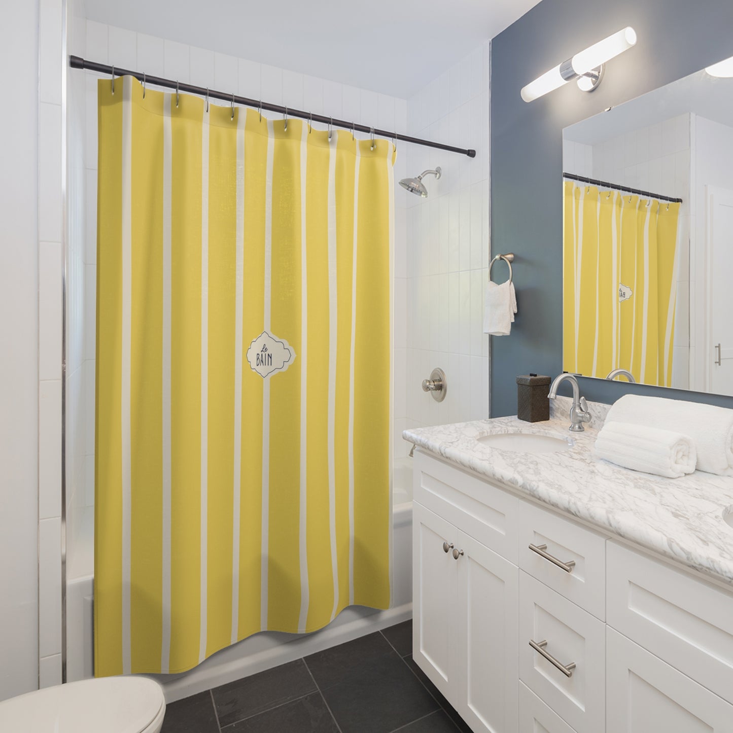 A yellow and white vertically striped shower curtain hanging in a modern white and blue-gray bathroom with a marble countertop, white vanity, and a mirror reflecting the curtain.