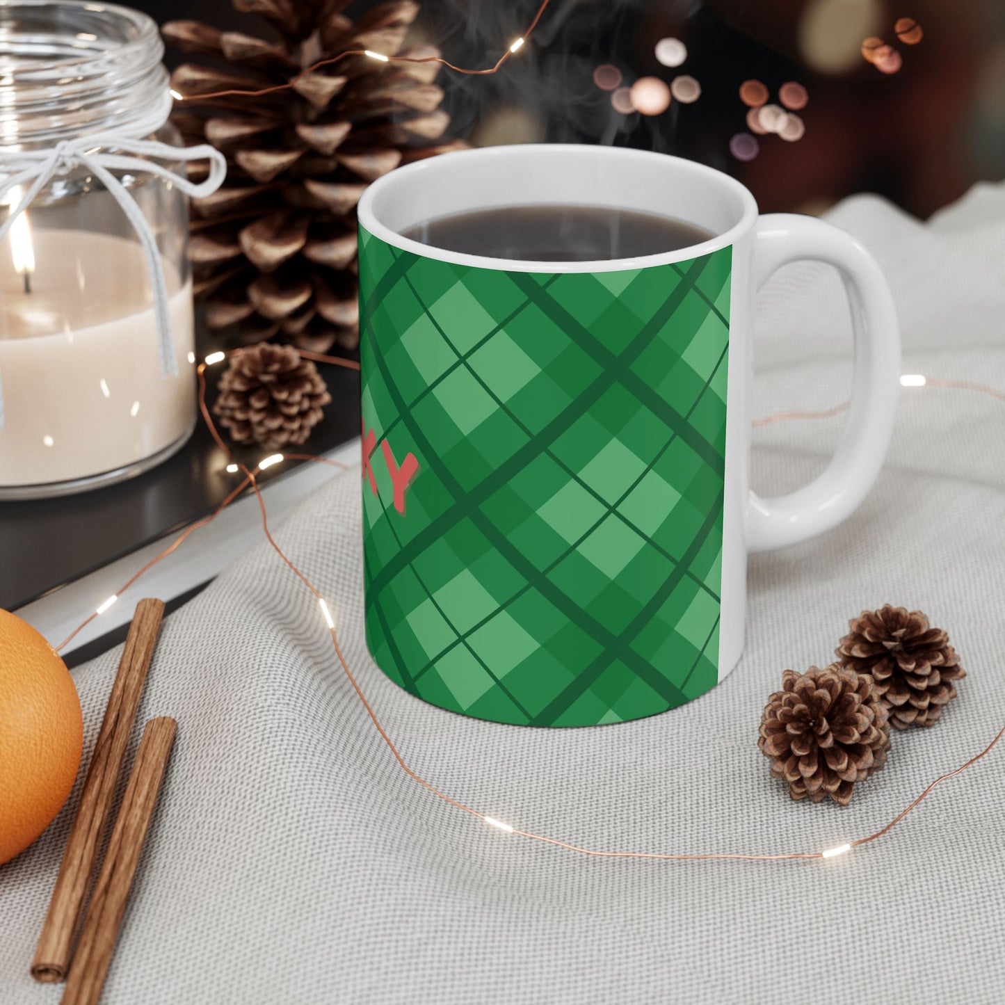 Green plaid mug with 'Merry' on a table with candles, oranges, and pinecones.