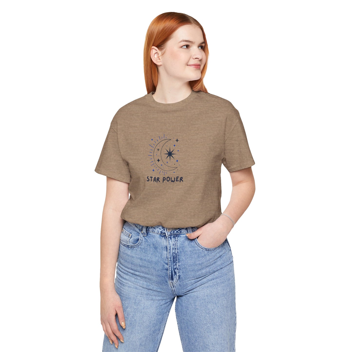 A woman with red hair wearing a heather brown t-shirt with a crescent moon and star graphic and the text 'STAR POWER' printed on the chest, paired with light blue jeans, against a plain white background.