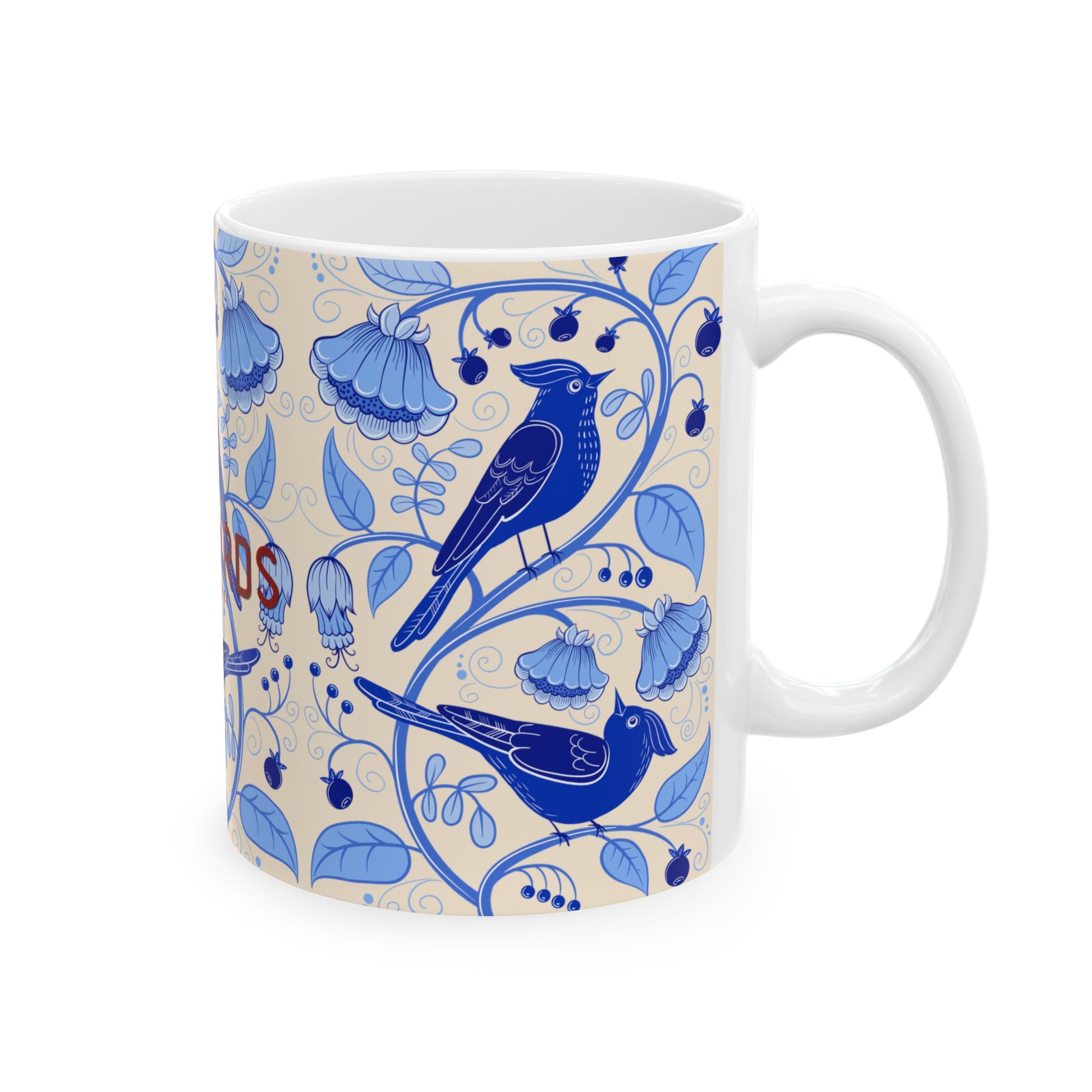 A white ceramic mug with a blue floral and bird pattern on a cream background, featuring two blue birds and blue flowers, with partial red text visible on the left side.