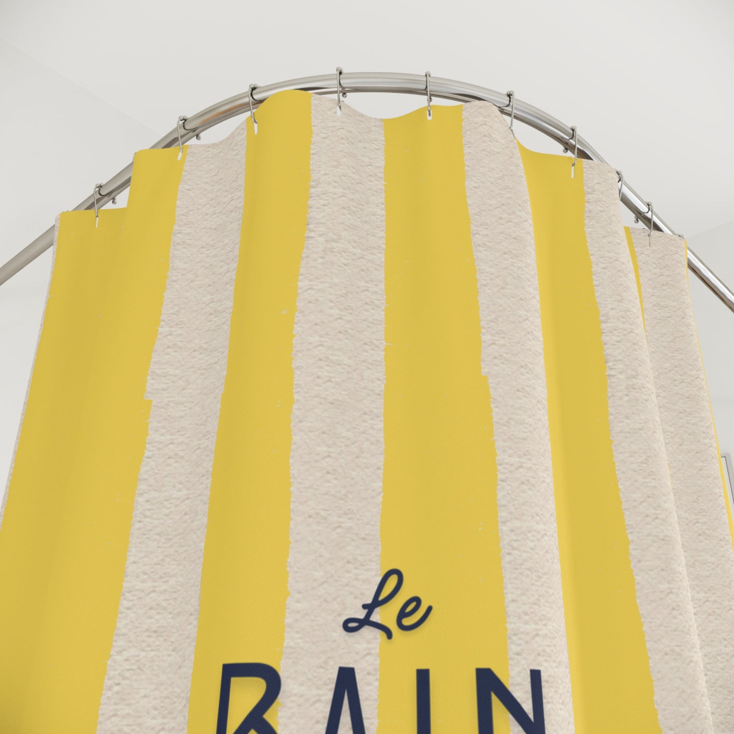 Yellow and gray striped towel with 'Le Bain' text on a metal rack against a white background