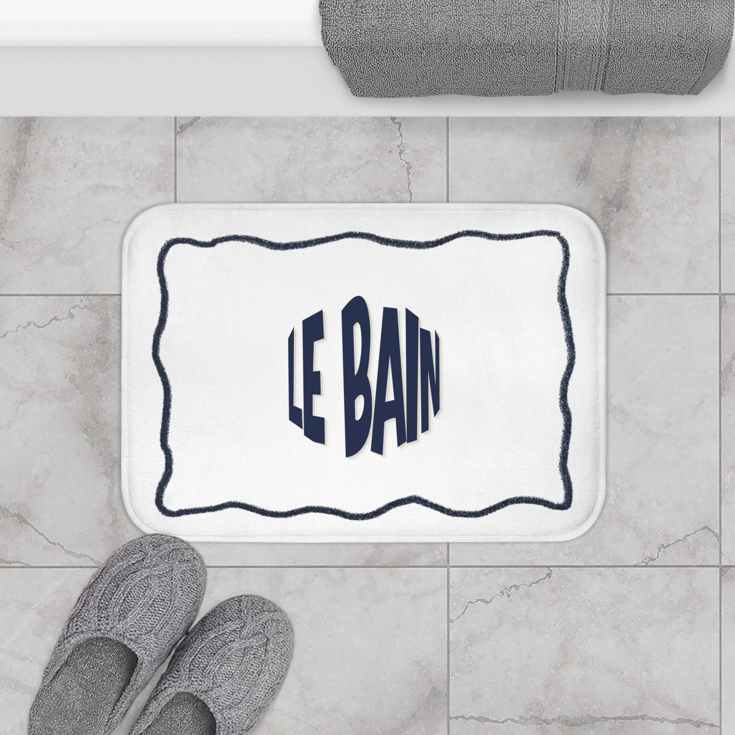 Bath mat with 'LE BAIN' text on a tiled bathroom floor.