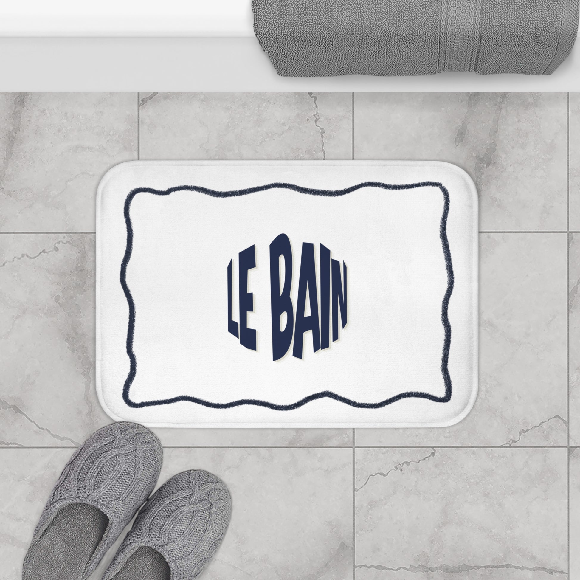 Bath mat with 'LE BAIN' text on a tiled bathroom floor.