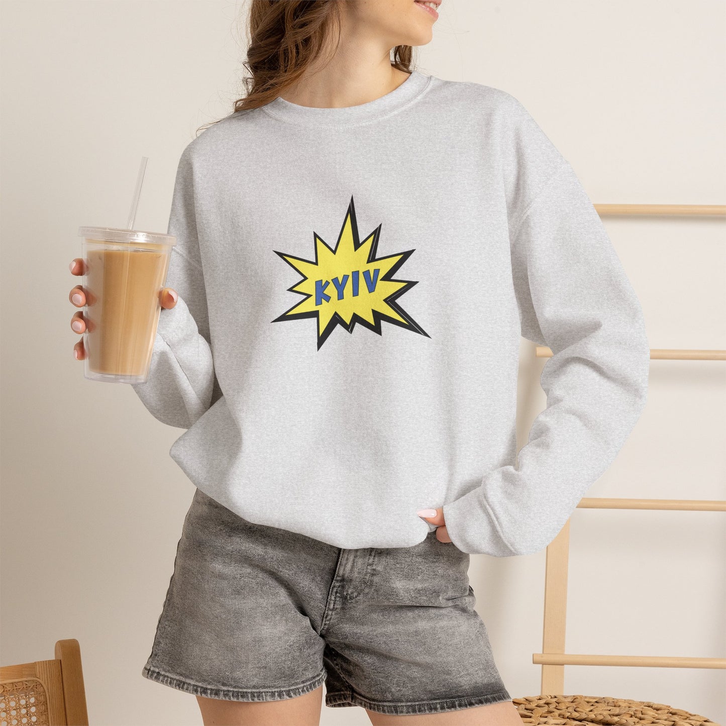 Person wearing a gray sweatshirt with a 'KYIV' design, holding a drink.