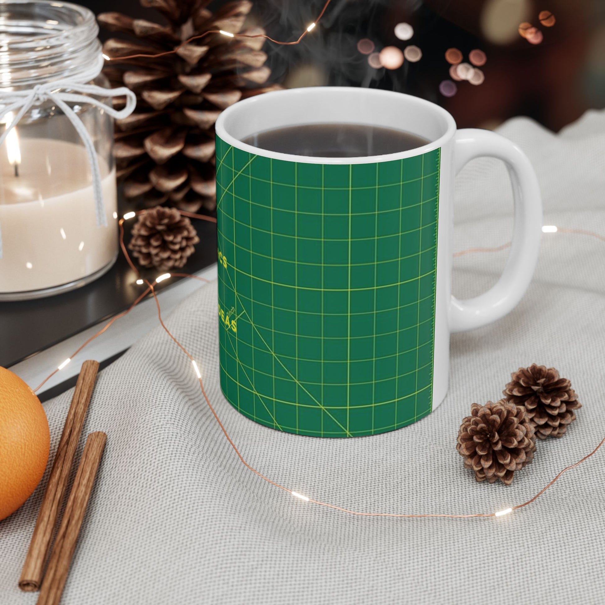 Green mug with grid pattern on a table with candles, oranges, and pine cones.