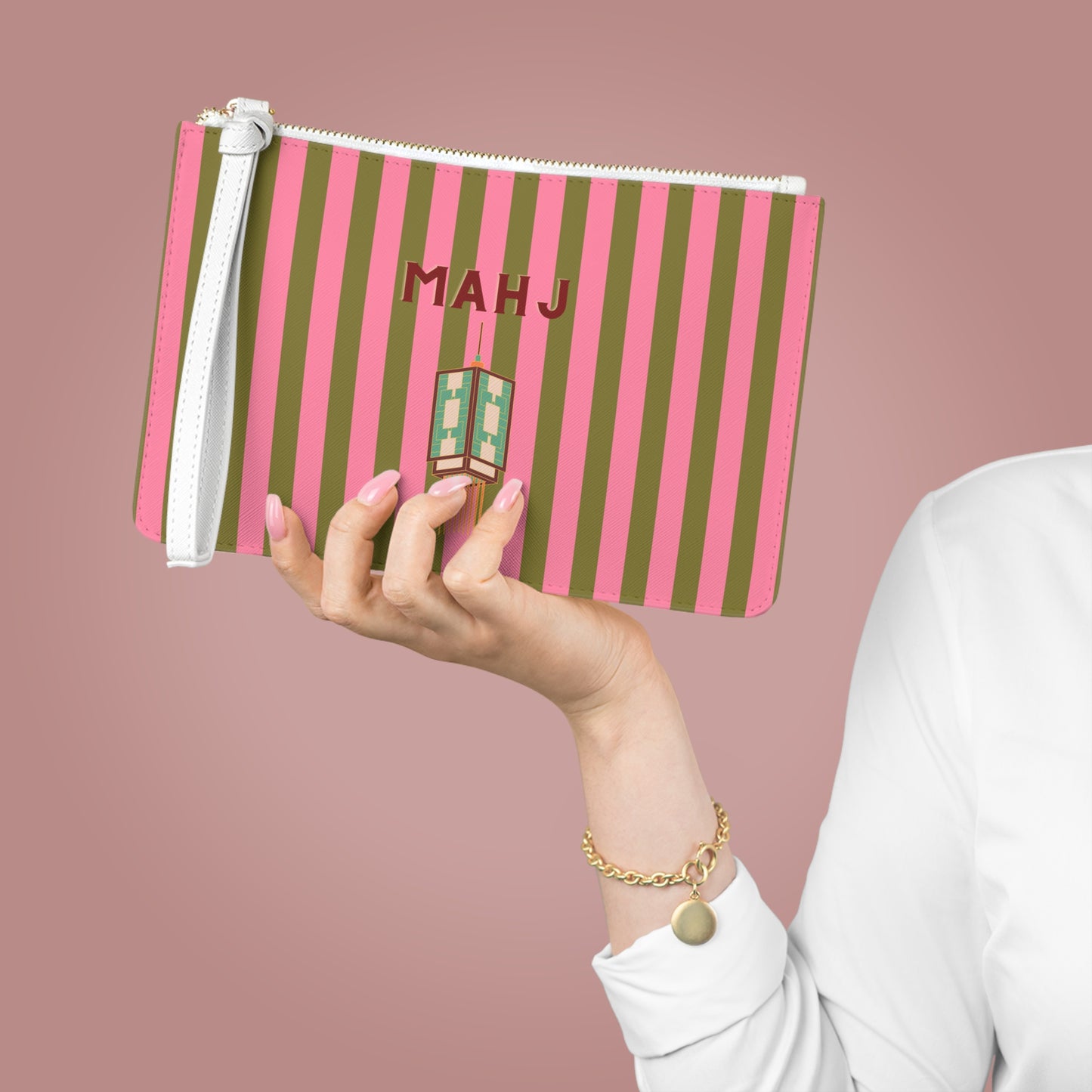 A hand holds a pink and olive green striped zipper pouch with a white wrist strap. The pouch features the name 'MAHJ' in red and a small lipstick-shaped charm.