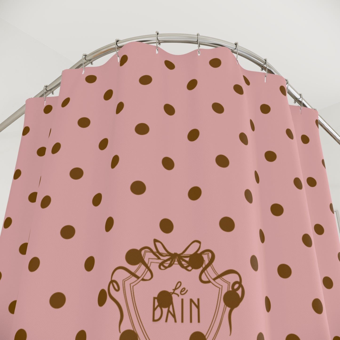 Pink shower curtain with brown polka dots and 'Le Bain' logo on a silver rod.