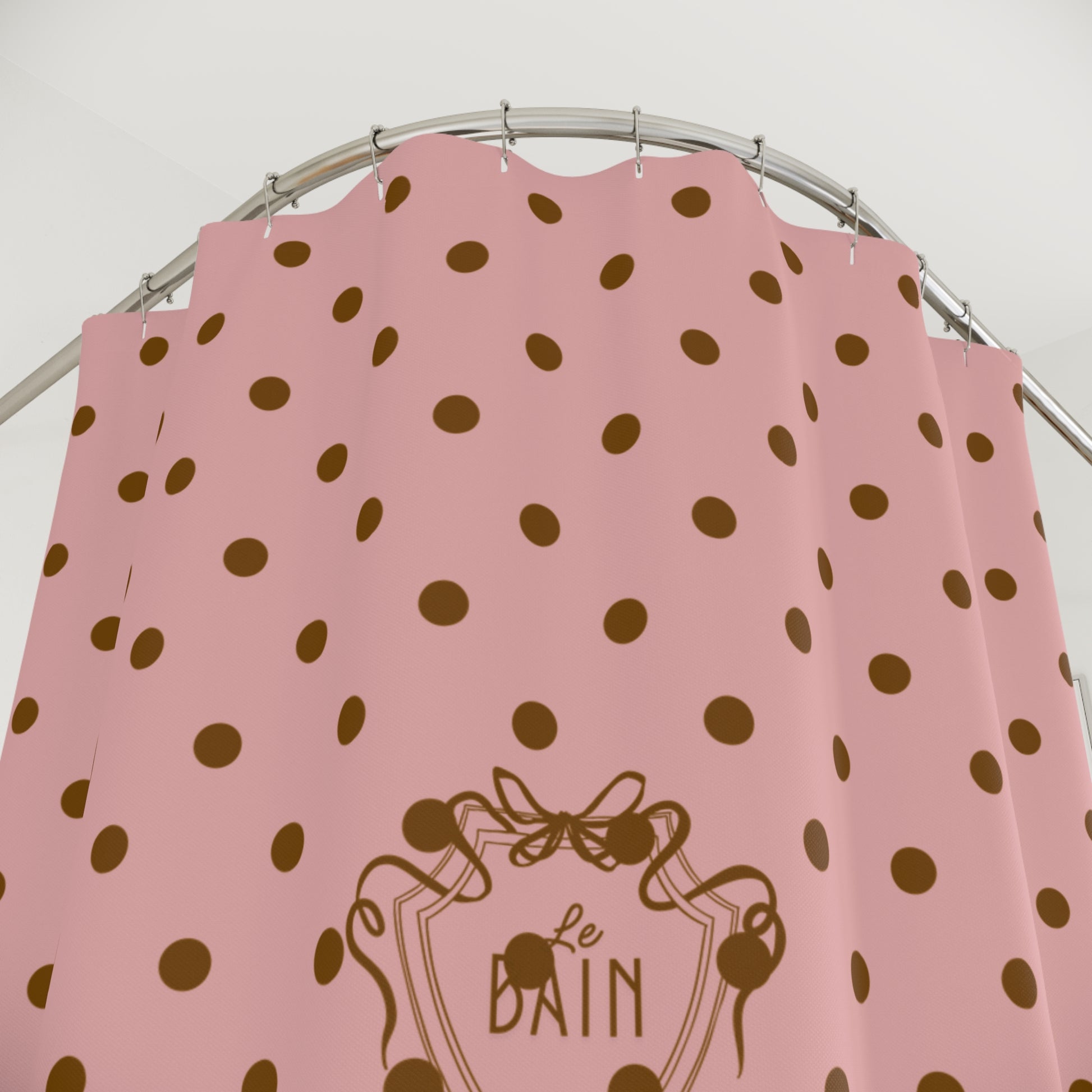 Pink shower curtain with brown polka dots and 'Le Bain' logo on a silver rod.
