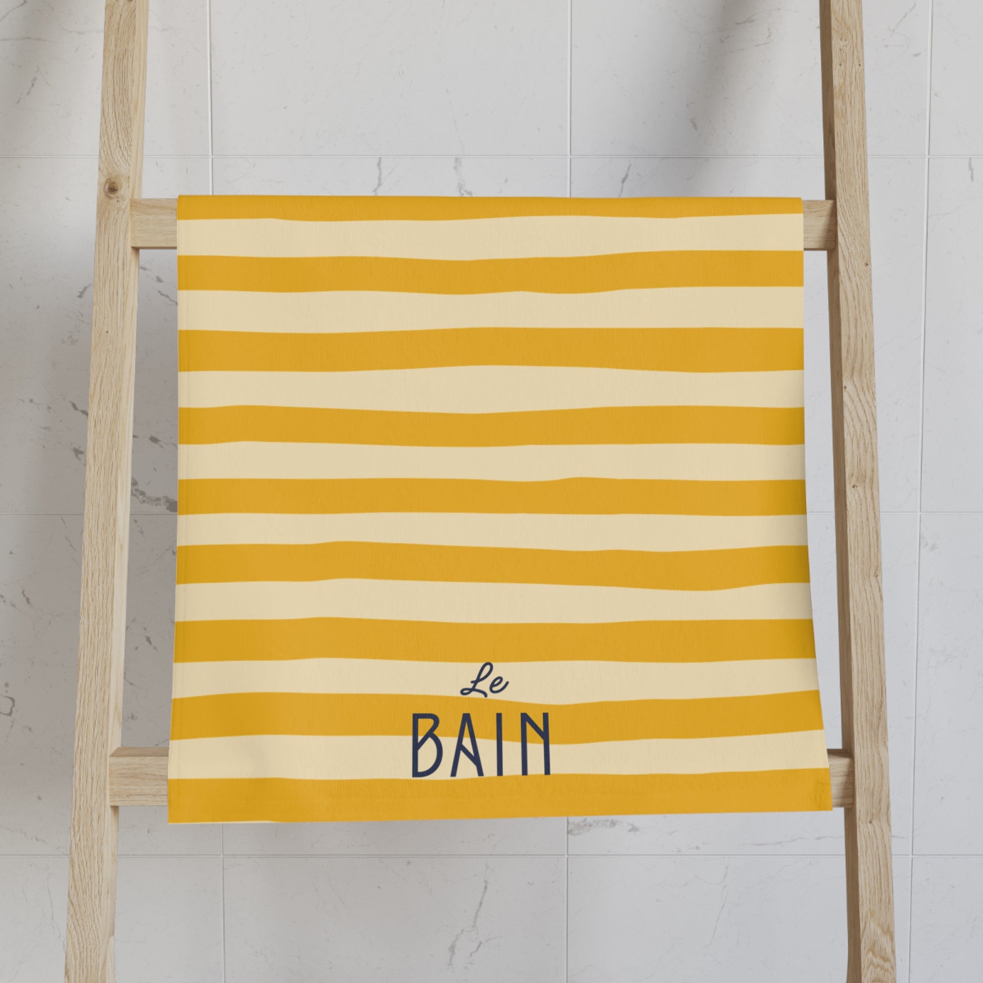 Yellow and white striped towel with 'Le Bain' text on a wooden ladder against a light background