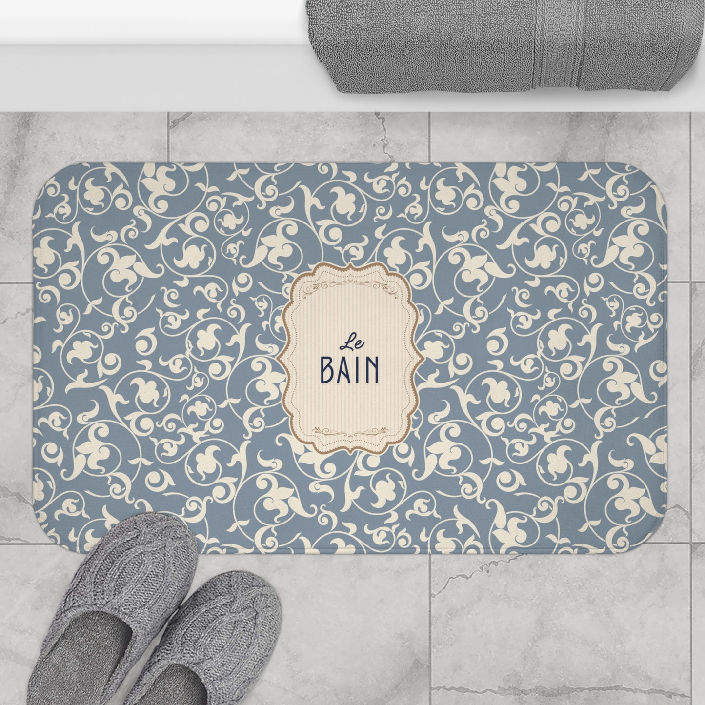 Decorative bath mat with floral pattern and 'Le Bain' text on a tiled floor.
