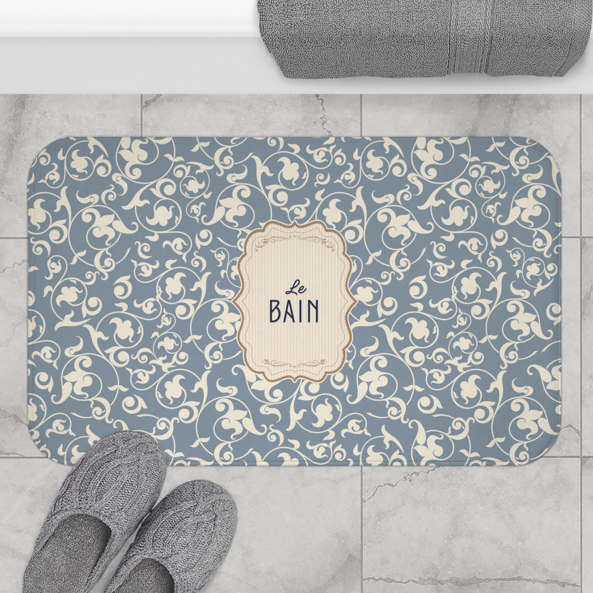 Decorative bath mat with floral pattern and 'Le Bain' text on a tiled floor.