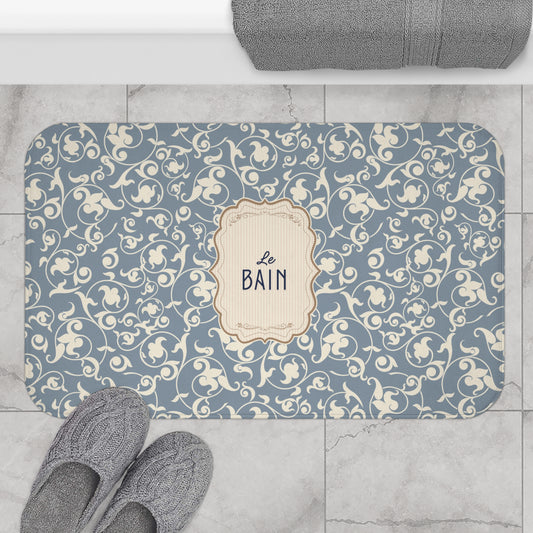 Decorative bath mat with floral pattern and 'Le Bain' text on a tiled floor.