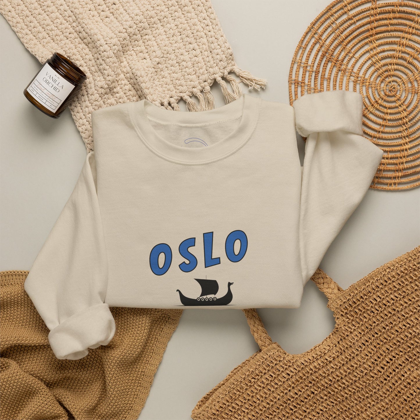 White sweatshirt with 'OSLO' print on a textured surface with a bottle and woven mat.