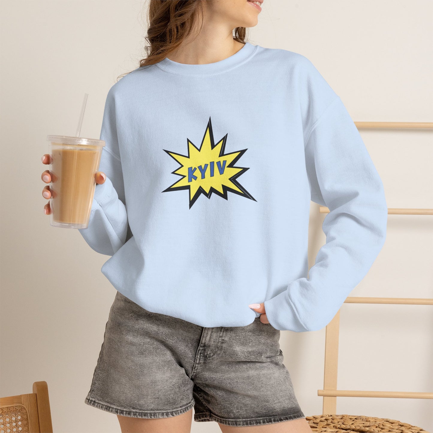 Person wearing a light blue sweatshirt with 'KYIV' design, holding a drink.