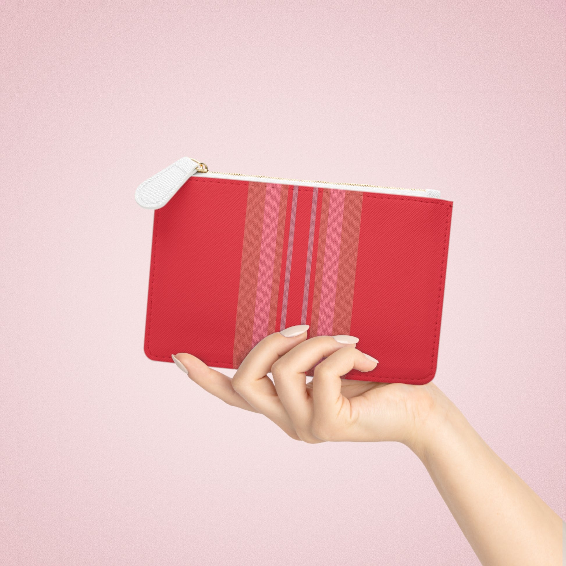 Hand holding a red pouch with pink stripes against a pink background