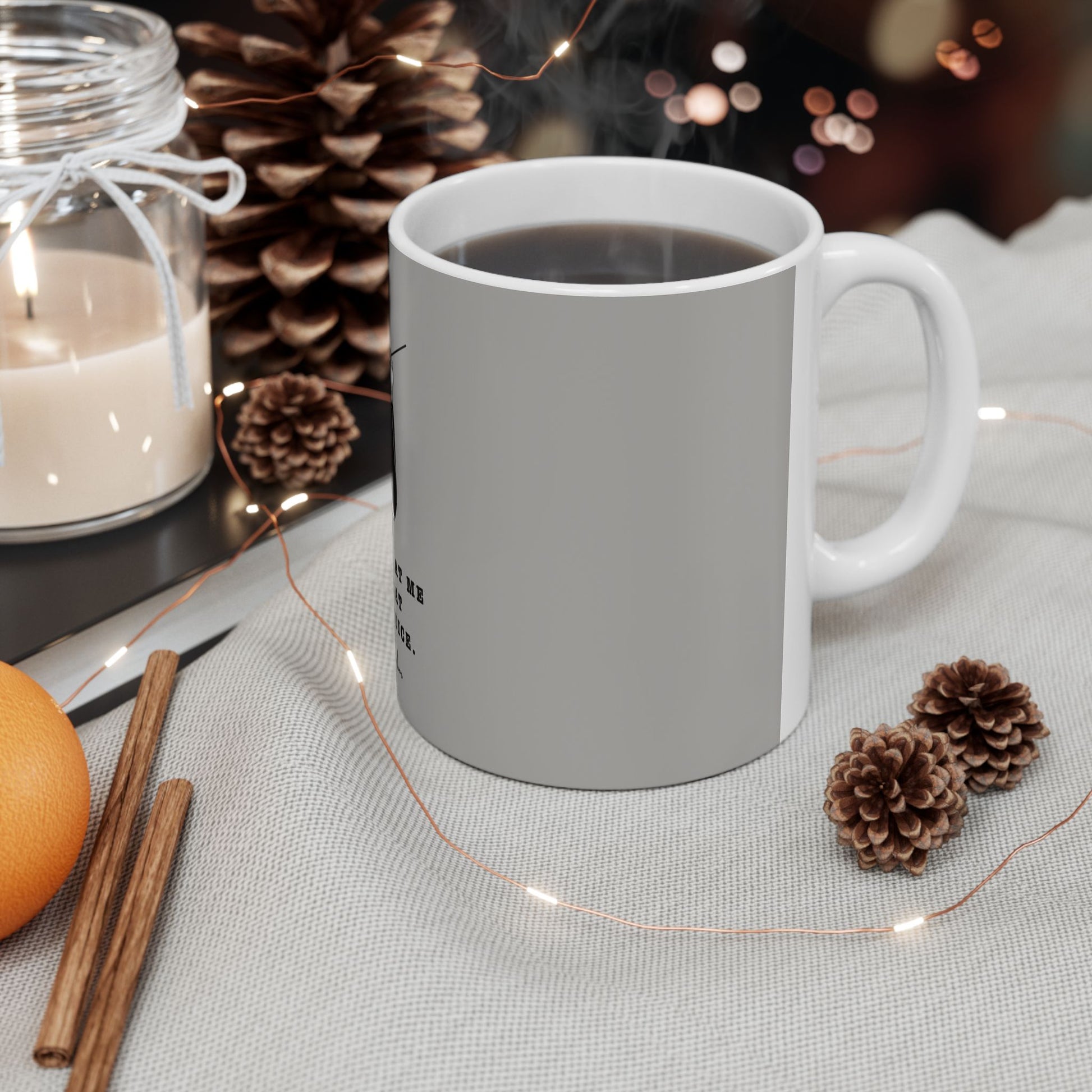 White mug with a decorative design on a table with candles, pinecones, and an orange.