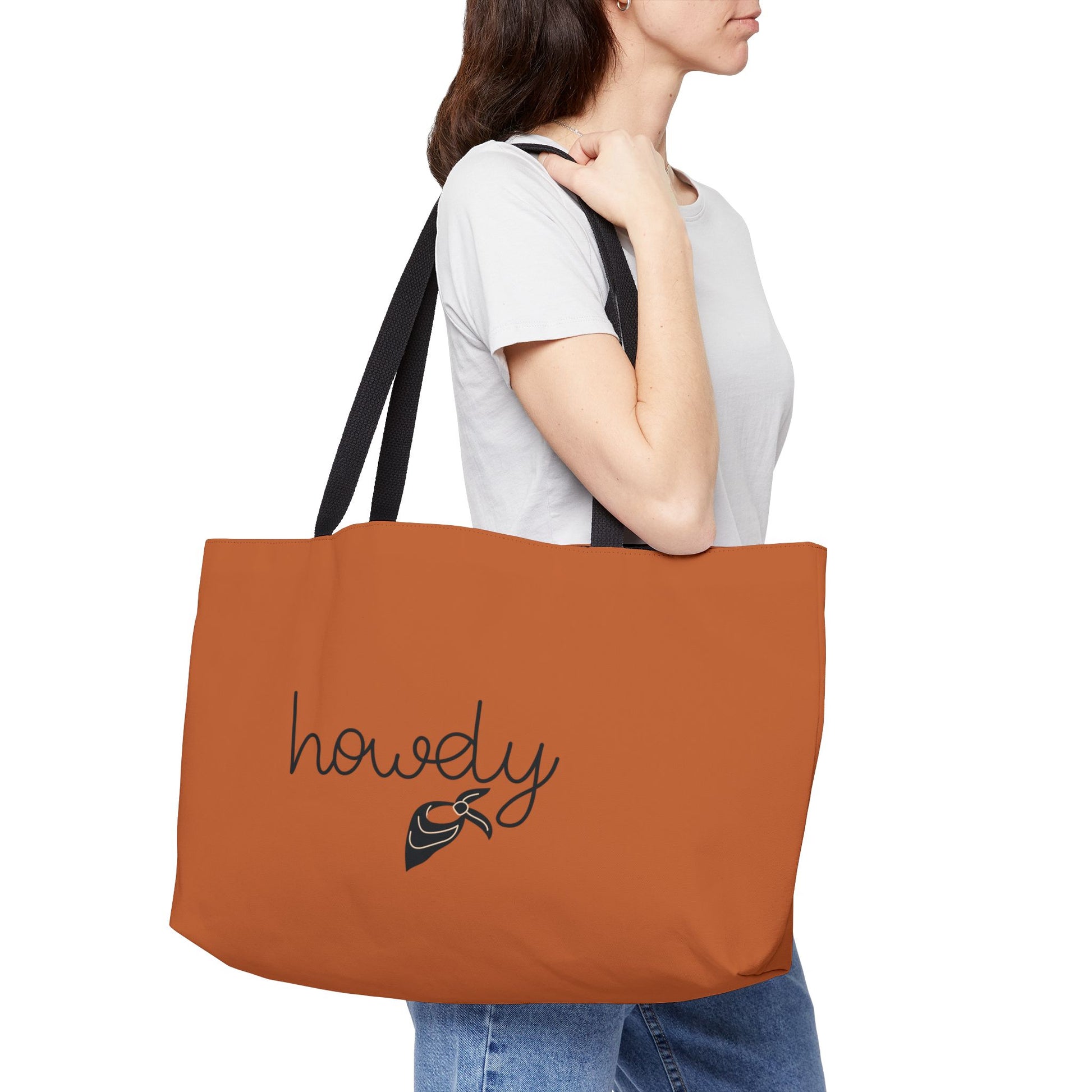 Person holding a brown tote bag with 'howdy' and a boot design on a white background