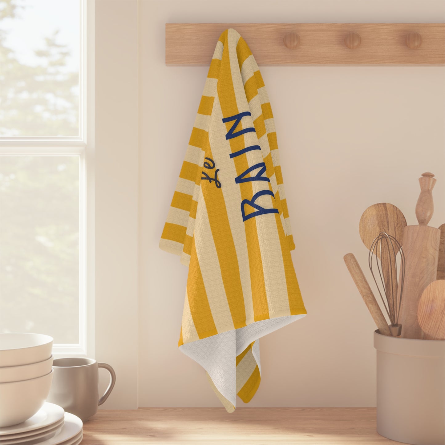 Yellow and white striped towel with blue text hanging on a wooden rack in a kitchen.