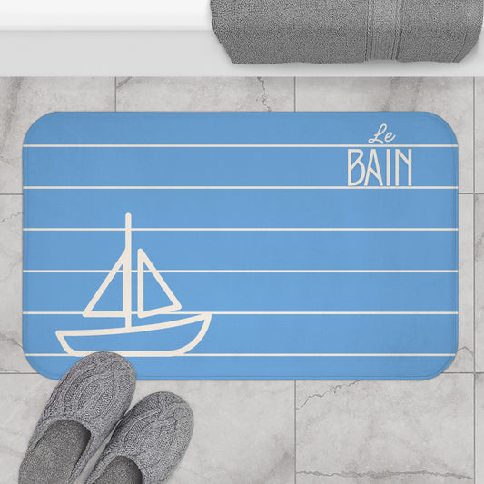 Blue bath mat with sailboat design and 'Le Bain' text on a bathroom floor.