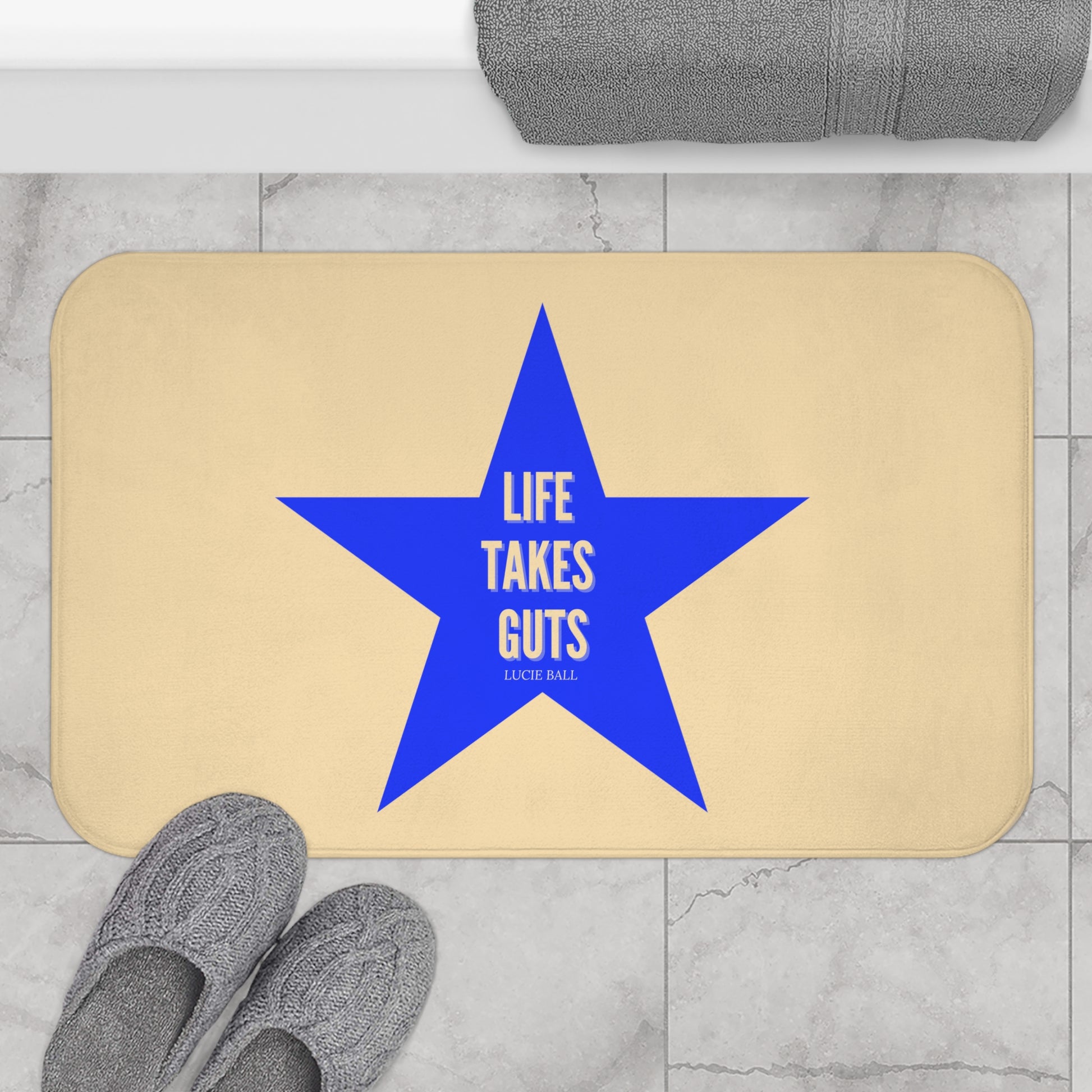 Beige doormat with a blue star and 'Life Takes Guts' text on a marble floor.