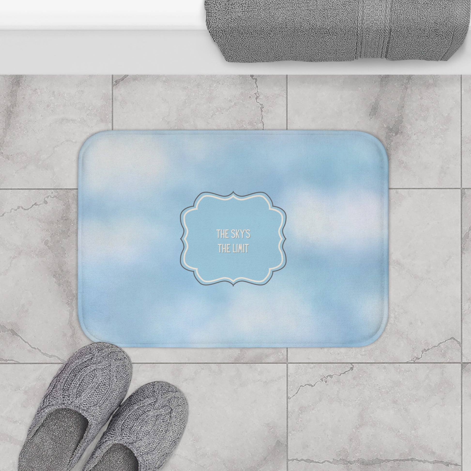 Blue bath mat with 'The Sky's the Limit' text on a marble floor.
