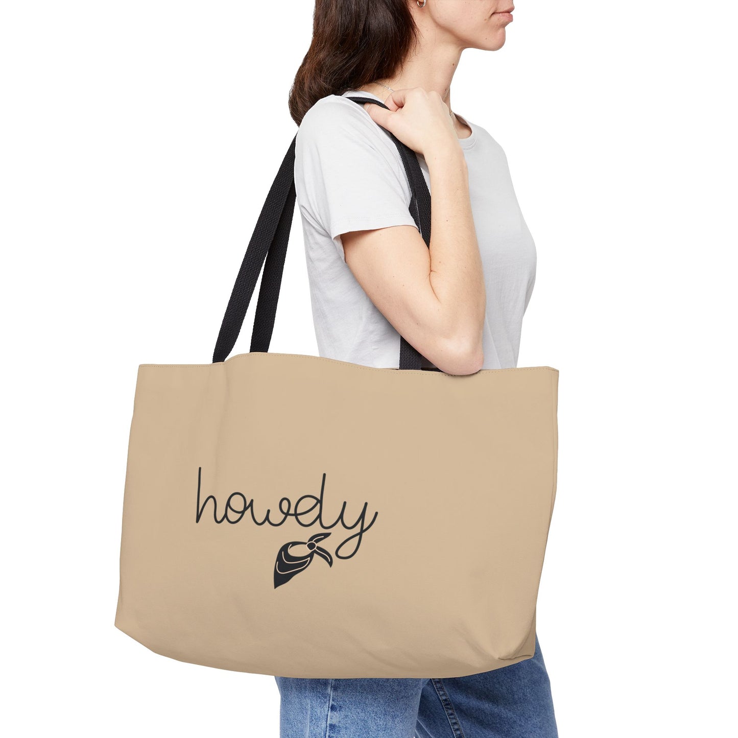 Person holding a beige tote bag with 'howdy' and a cowboy hat design.