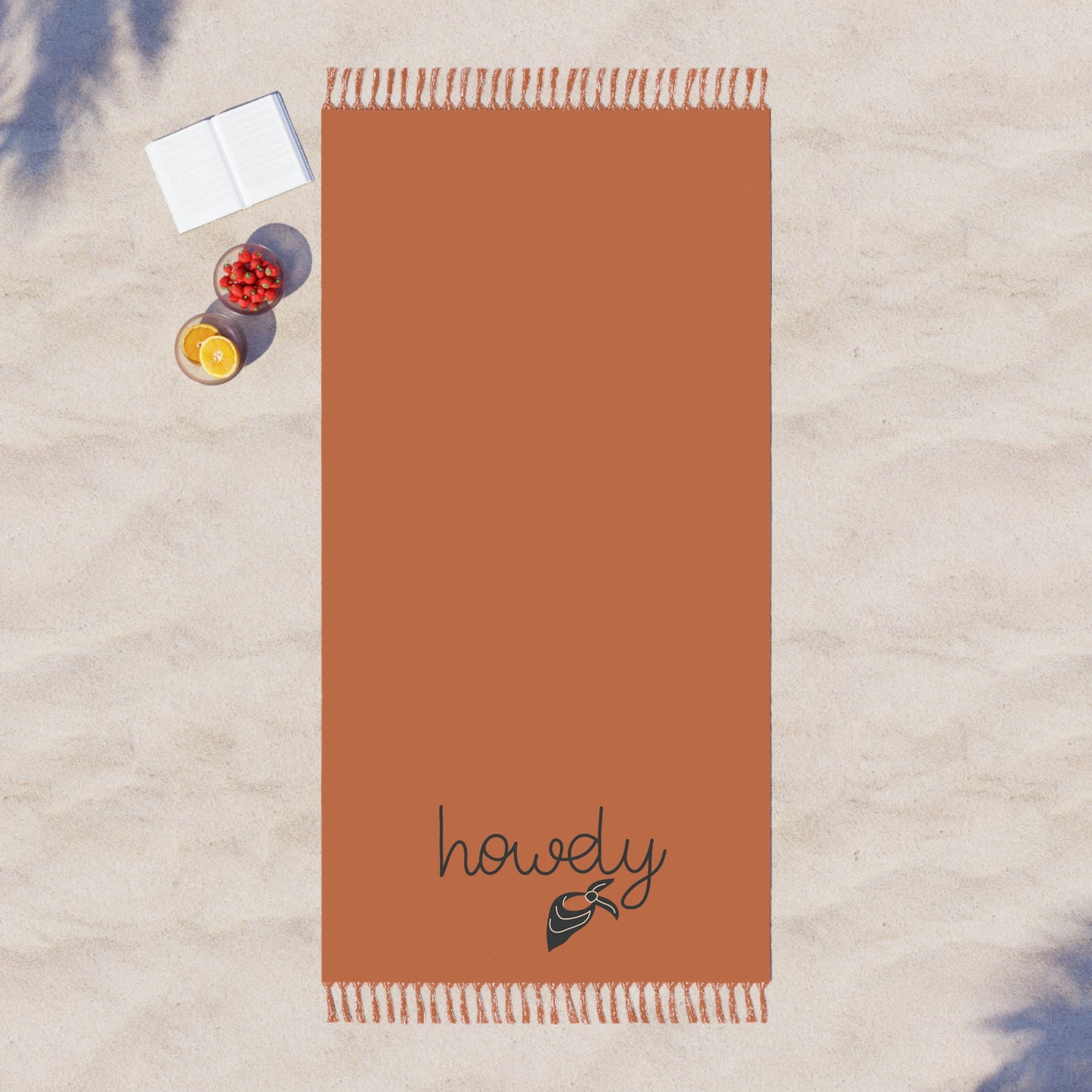 Brown towel with 'howdy' embroidery on a sandy surface