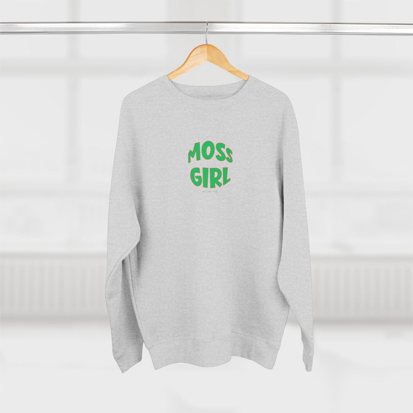 Gray sweatshirt with 'MOSS GIRL' text in green on a wooden hanger against a white background
